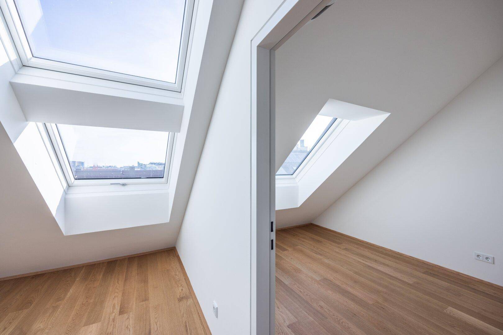 Zwei helle Räume im Dachgeschoss mit Holzboden und großen Dachfenstern, bieten Weitblick.