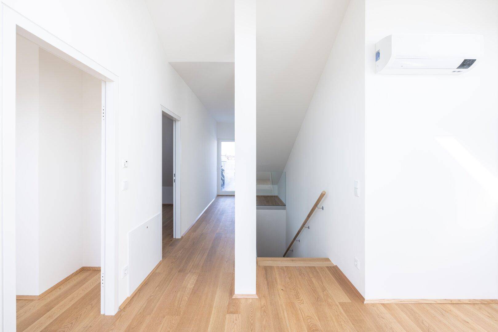 Heller Flur im Dachgeschoss mit Holzboden und Klimaanlage, führt zu weiteren Räumen und Treppe.