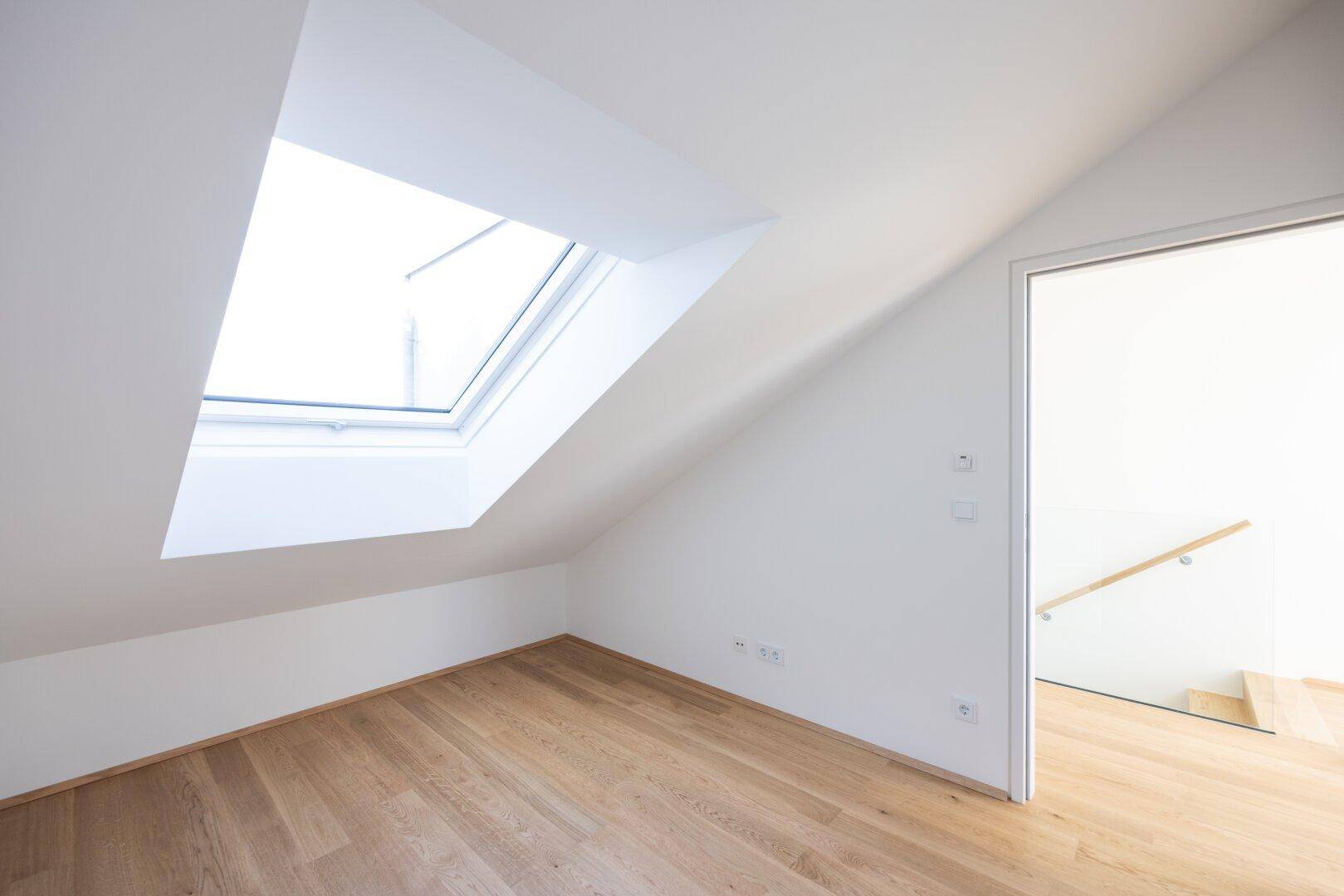 Heller Raum im Dachgeschoss mit Holzboden und großem Dachfenster, bietet viel natürliches Licht.