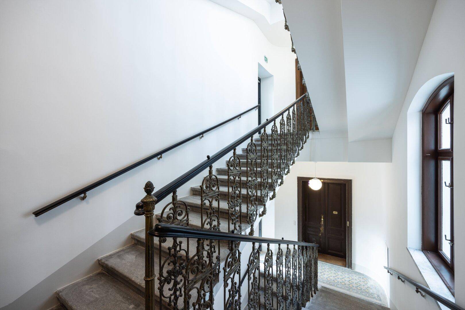 Historisches Treppenhaus mit kunstvollem schmiedeeisernem Geländer und hohen Decken.