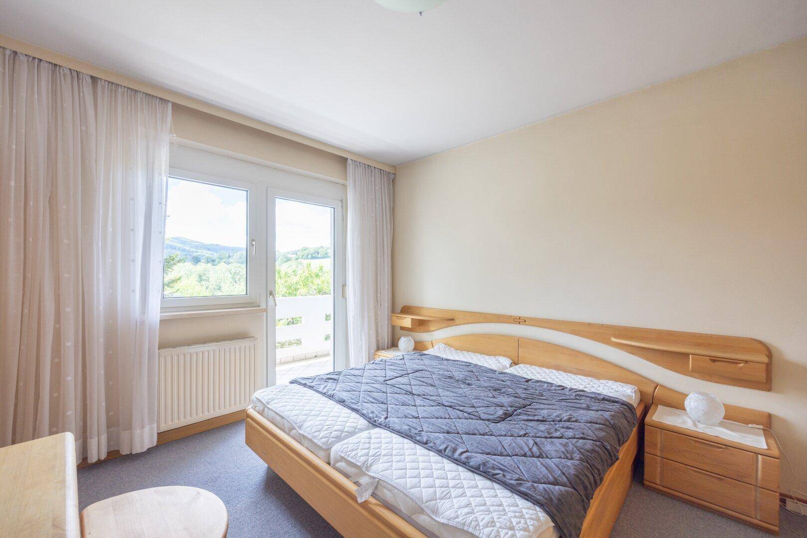 Schlafzimmer mit Doppelbett, Teppichboden und Zugang zu einem Balkon mit Weitblick.