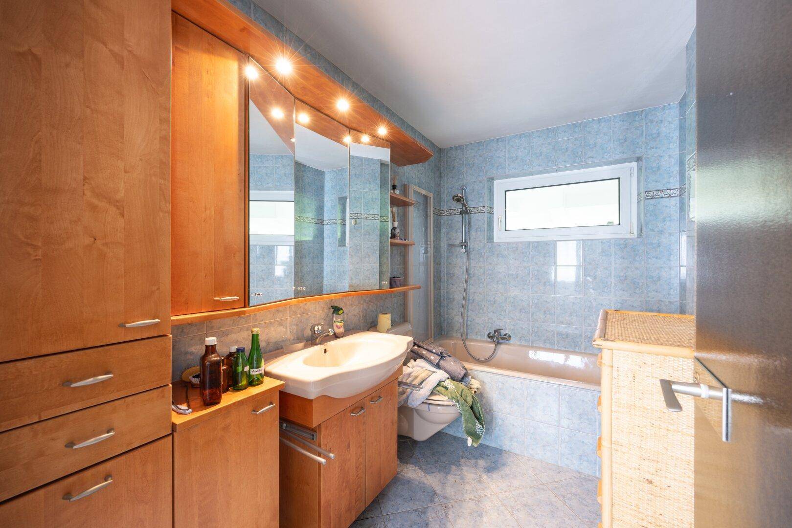 Badezimmer mit Badewanne, Waschbecken, Spiegelschrank und blauen Fliesen.