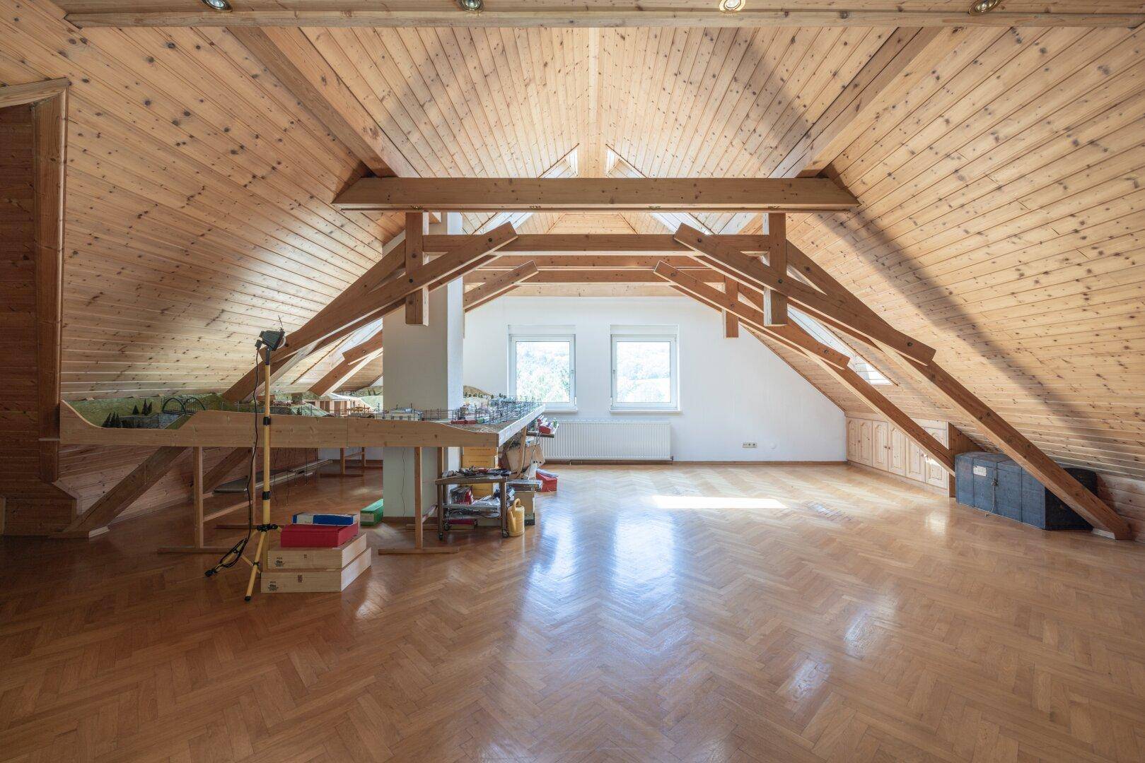 Geräumiger Dachbodenraum mit sichtbaren Holzbalken, Holzverkleidung und Fischgrätparkett.