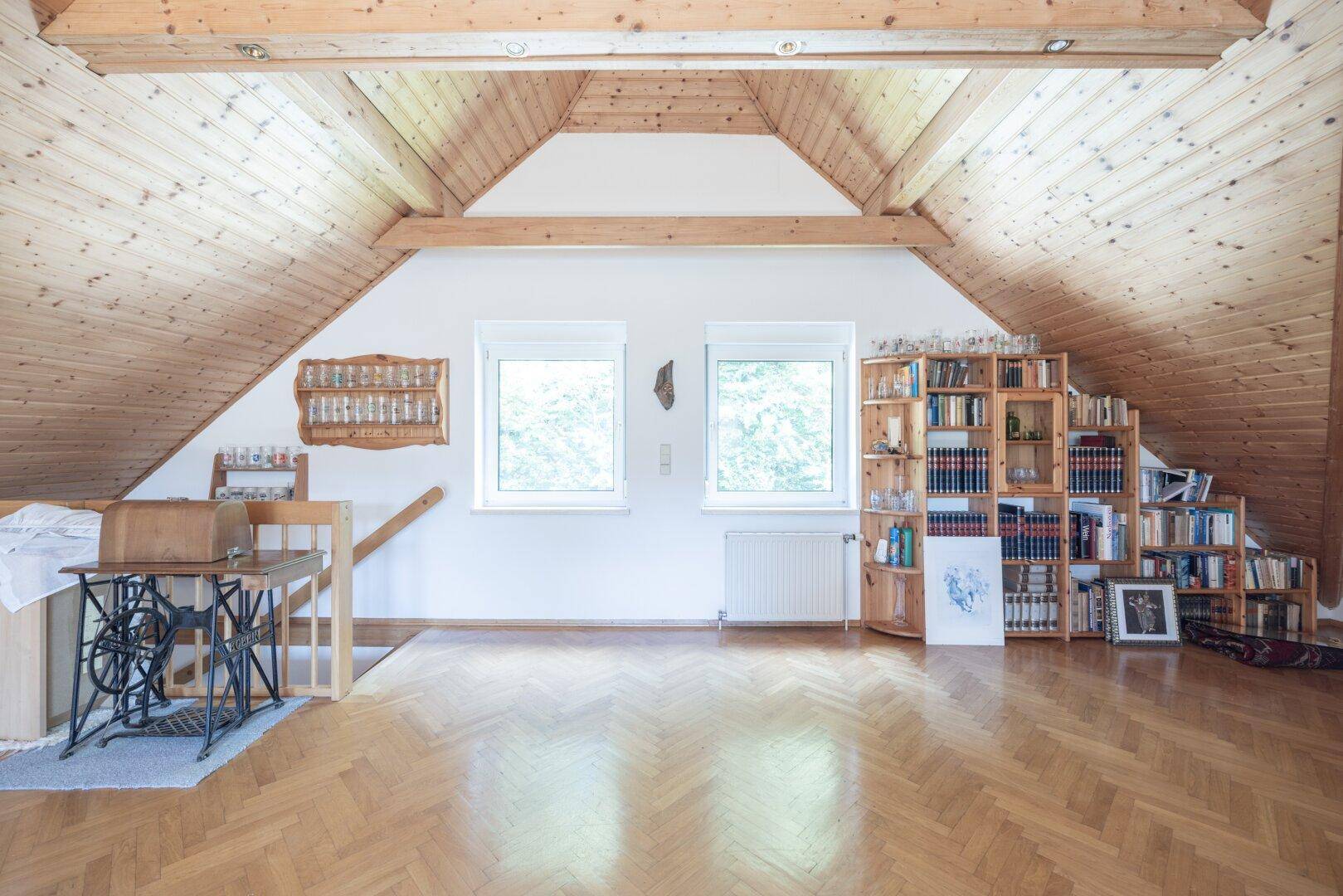 Heller Dachbodenraum mit Holzbalken, Fenstern und einem Bücherregal, ideal als Hobbyraum.