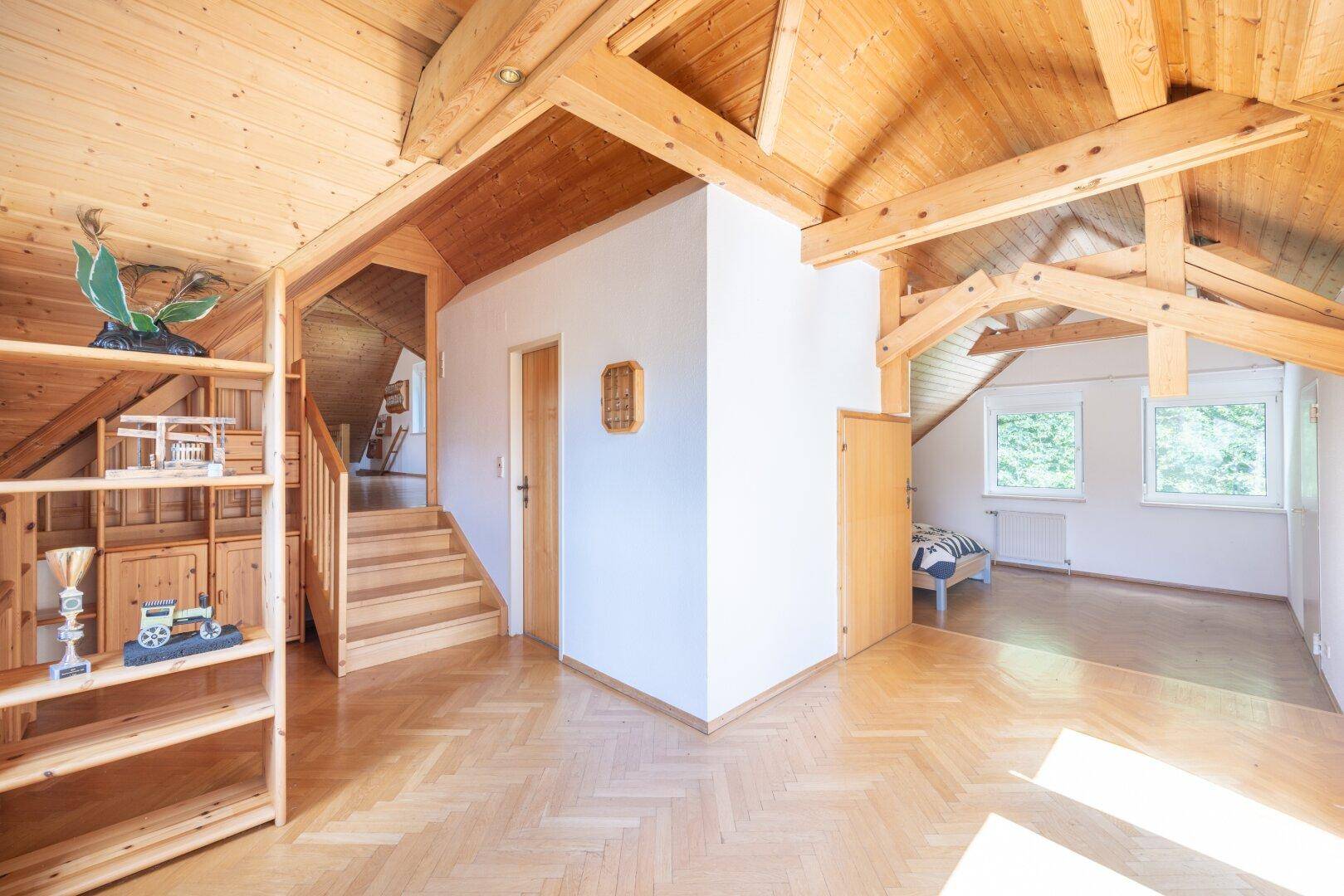 Flur im Dachgeschoss mit Holztreppe, Regalen und Holzboden, der zu weiteren Räumen führt.