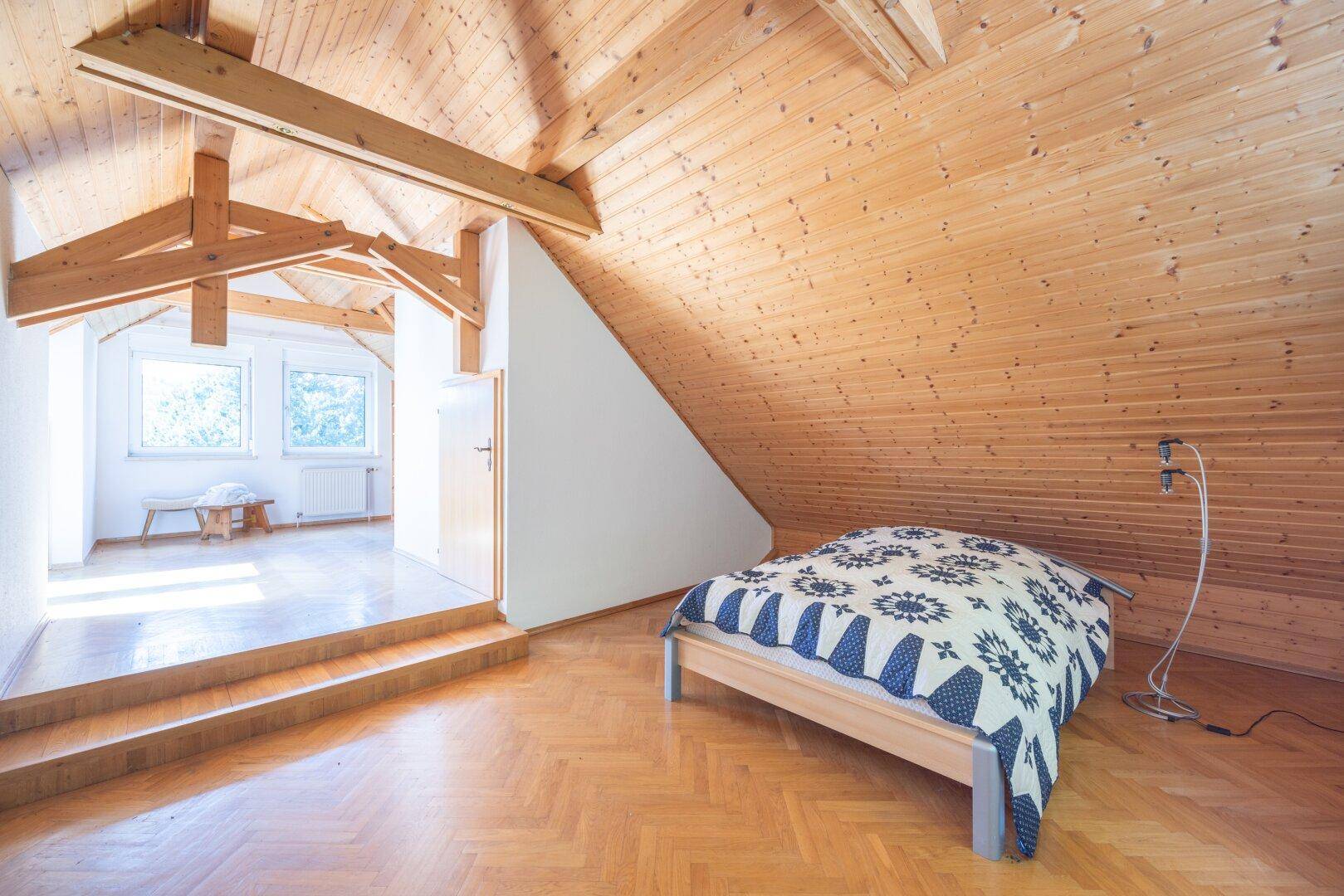 Schlafzimmer im Dachgeschoss mit Holzboden, schräger Decke und natürlichem Lichteinfall.