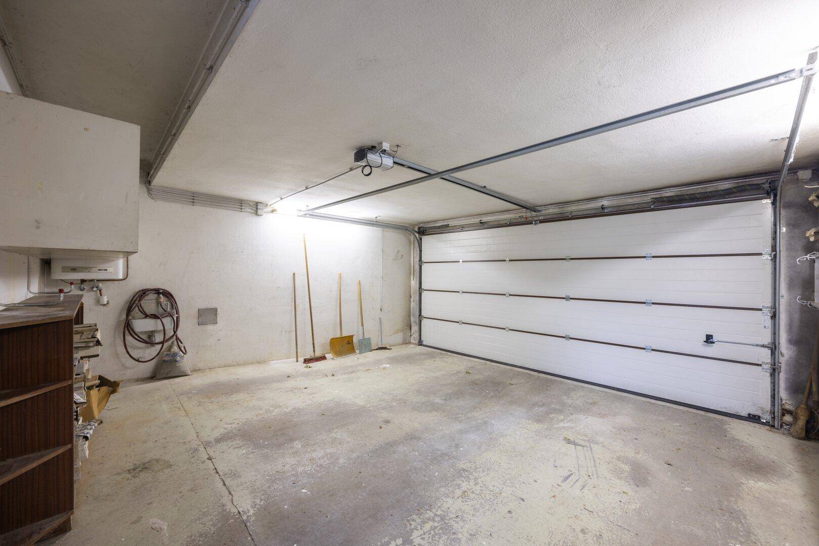 Geräumige Garage mit weißem Sektionaltor und Betonboden, bietet Platz für Fahrzeuge.