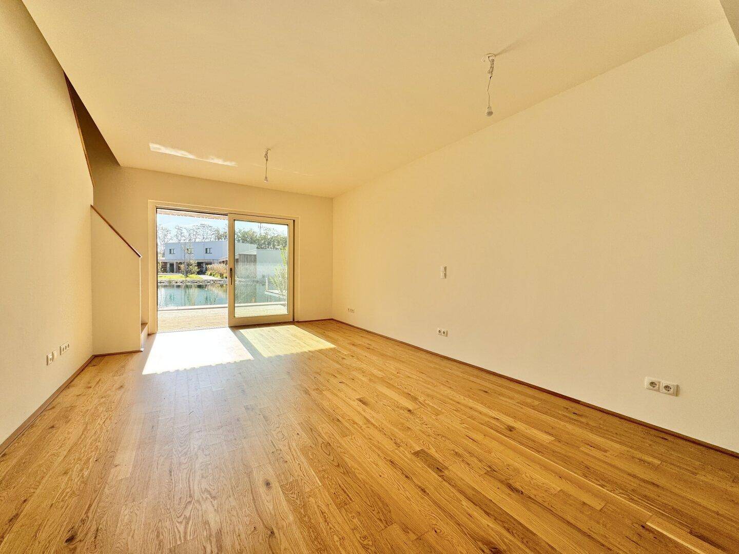 Helles Wohnzimmer mit Eichenparkett und großer Schiebetür, die direkten Zugang zur Seeterrasse bietet.