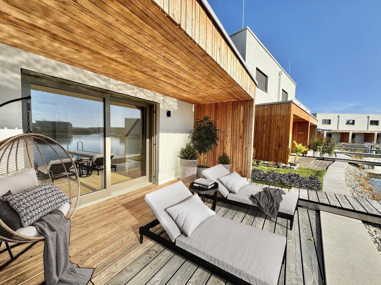Möblierte Holzterrasse mit Liegestühlen und Hängesessel, bietet direkten Zugang zum Haus und Seeblick.