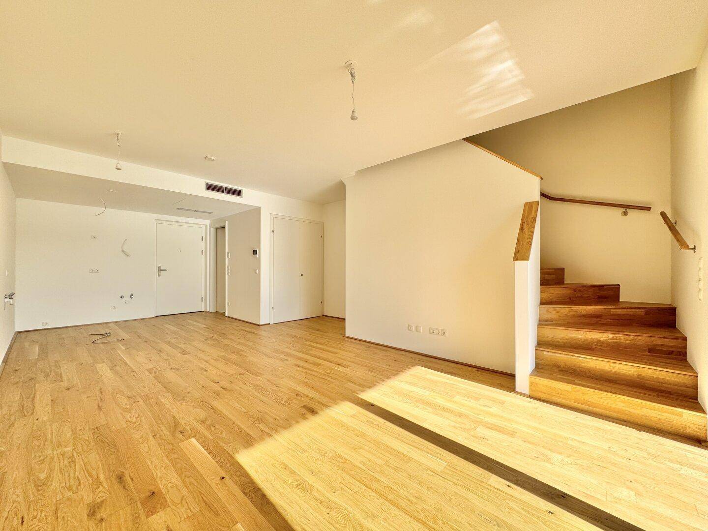 Geräumiger Wohnbereich mit hellem Eichenparkett und offener Treppe, bereit für individuelle Gestaltung.