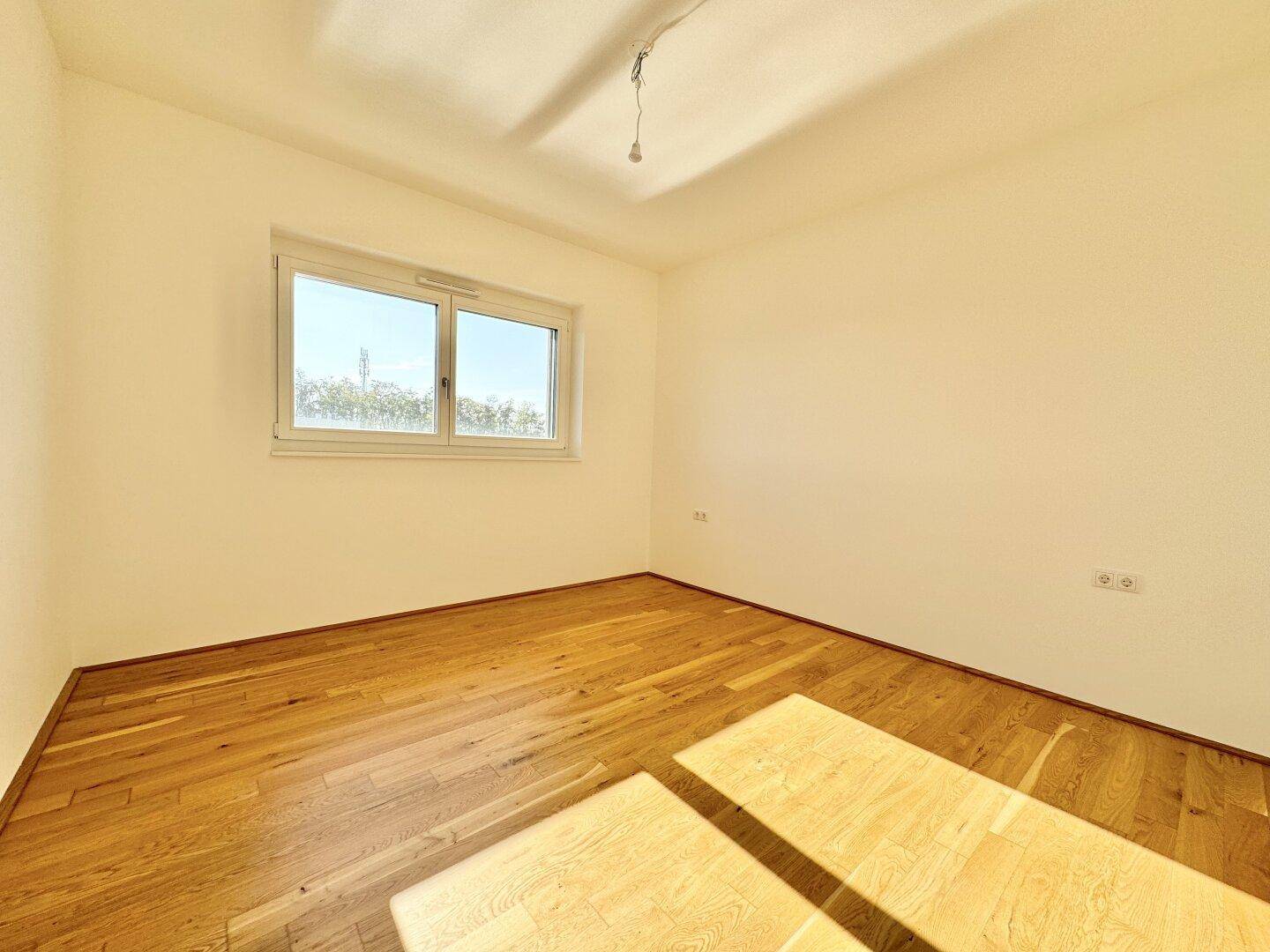 Helles Schlafzimmer mit Eichenparkett und großem Fenster, bietet viel natürliches Licht und eine angenehme Atmosphäre.
