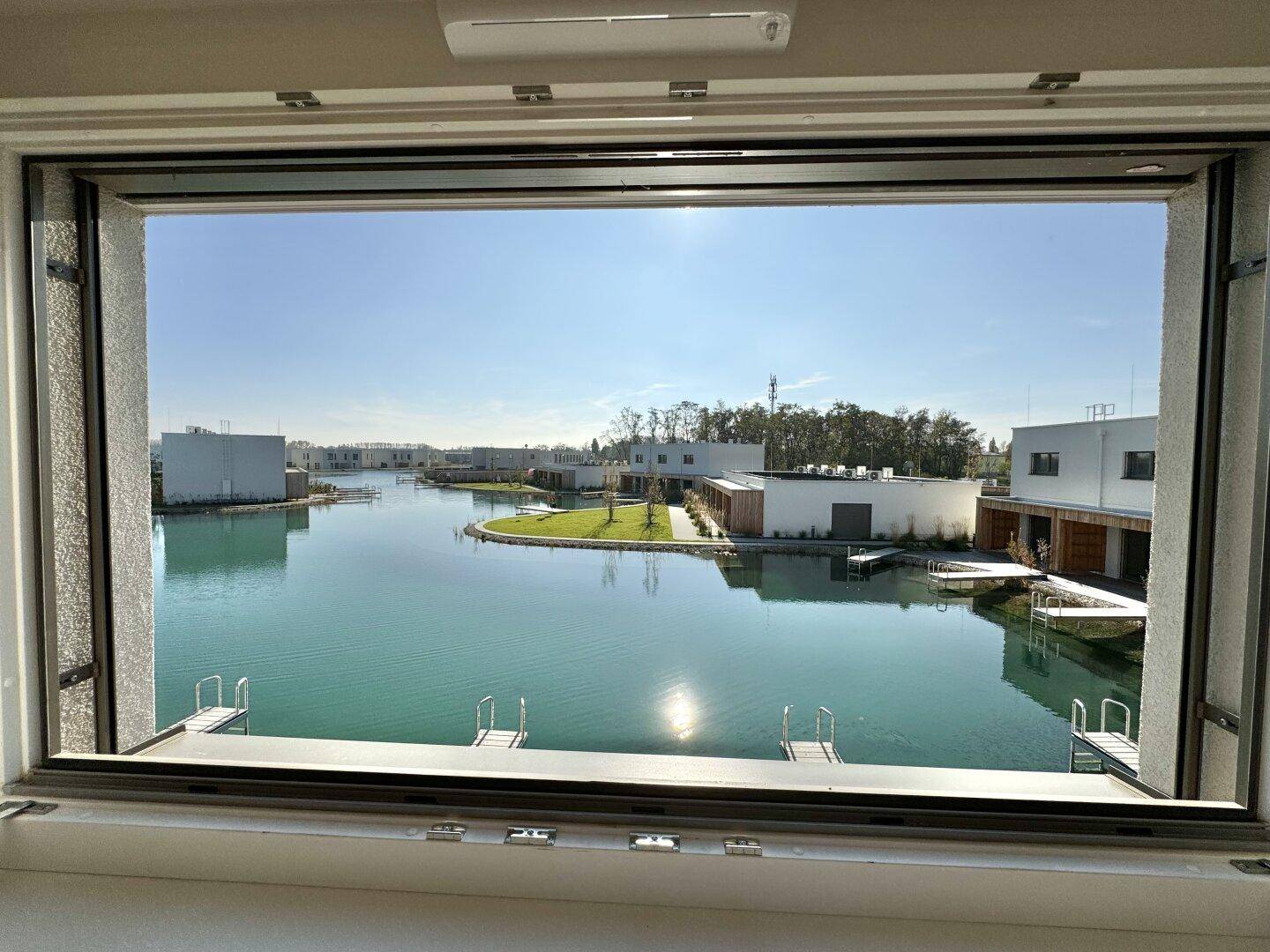Panoramablick aus dem Fenster auf die ruhige Seenlandschaft und die modernen Häuser der Siedlung.