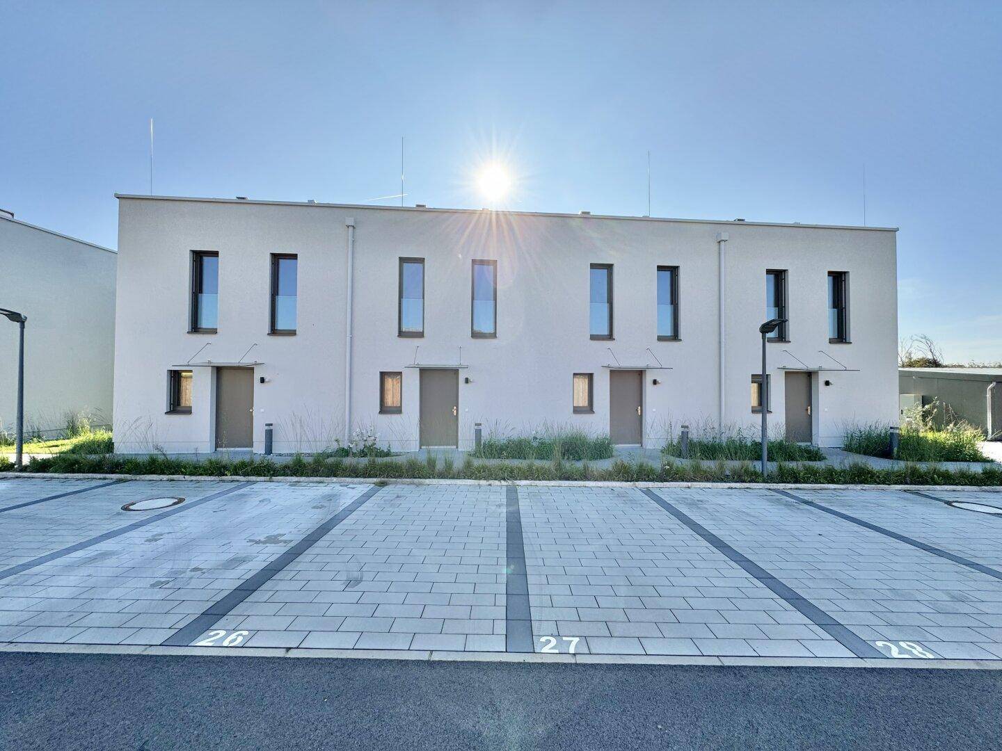 Moderne Reihenhäuser mit klaren Linien und privaten Parkplätzen vor der Fassade unter blauem Himmel.