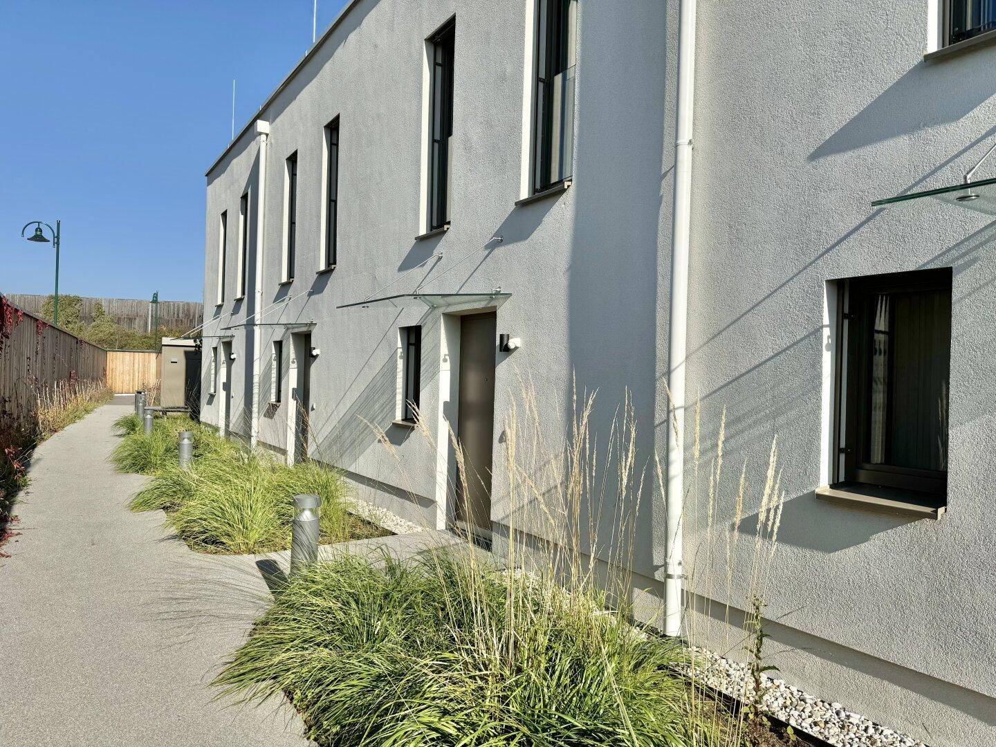 Seitenansicht der modernen Gebäude mit gepflegtem Gehweg und grüner Bepflanzung entlang der Fassade.