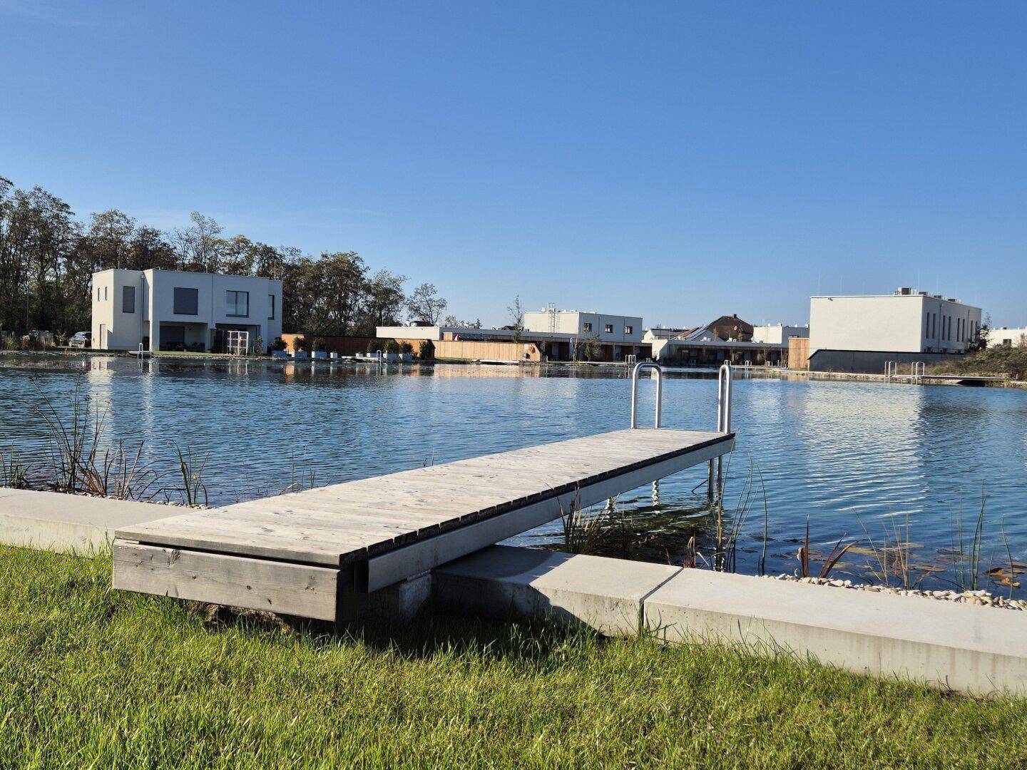 Holzsteg am Seeufer mit Blick auf weitere moderne Häuser in der Ferne.