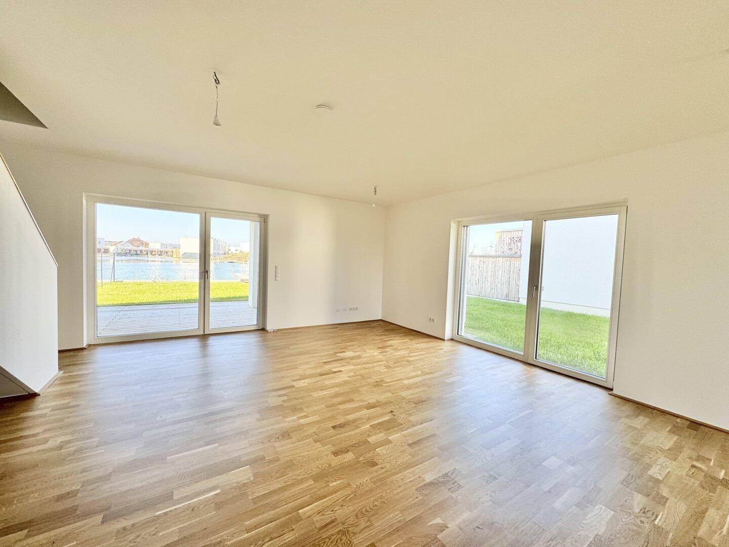 Helles Wohnzimmer mit Parkettboden und großen Fenstern mit Blick auf den See und Garten.