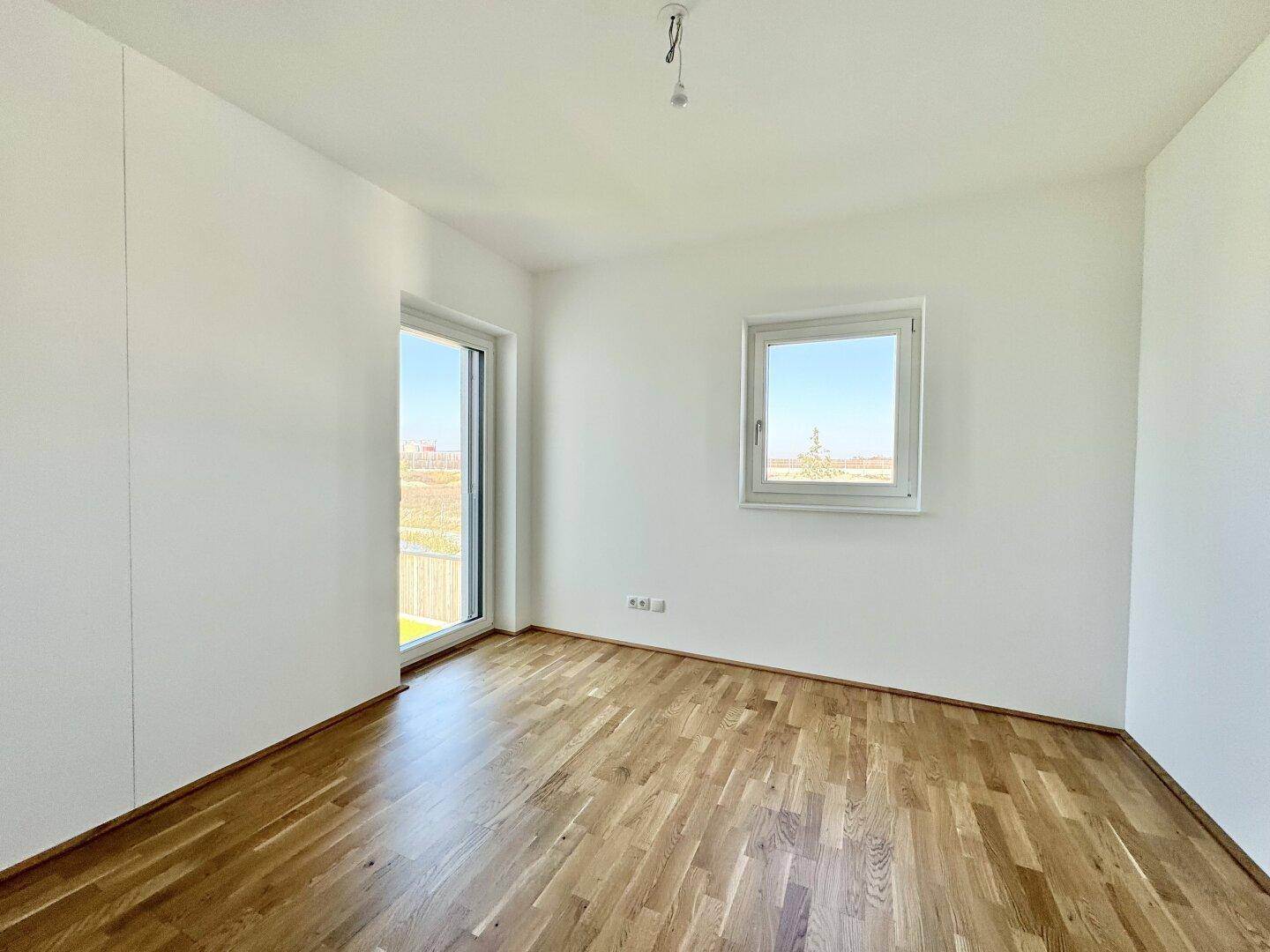 Heller Raum mit Parkettboden und Zugang zu einem kleinen Außenbereich.