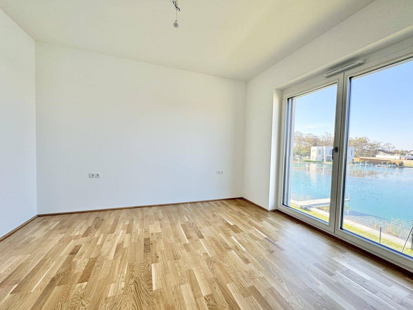 Schlafzimmer mit Parkettboden und raumhohen Fenstern, die einen weiten Blick auf den See bieten.