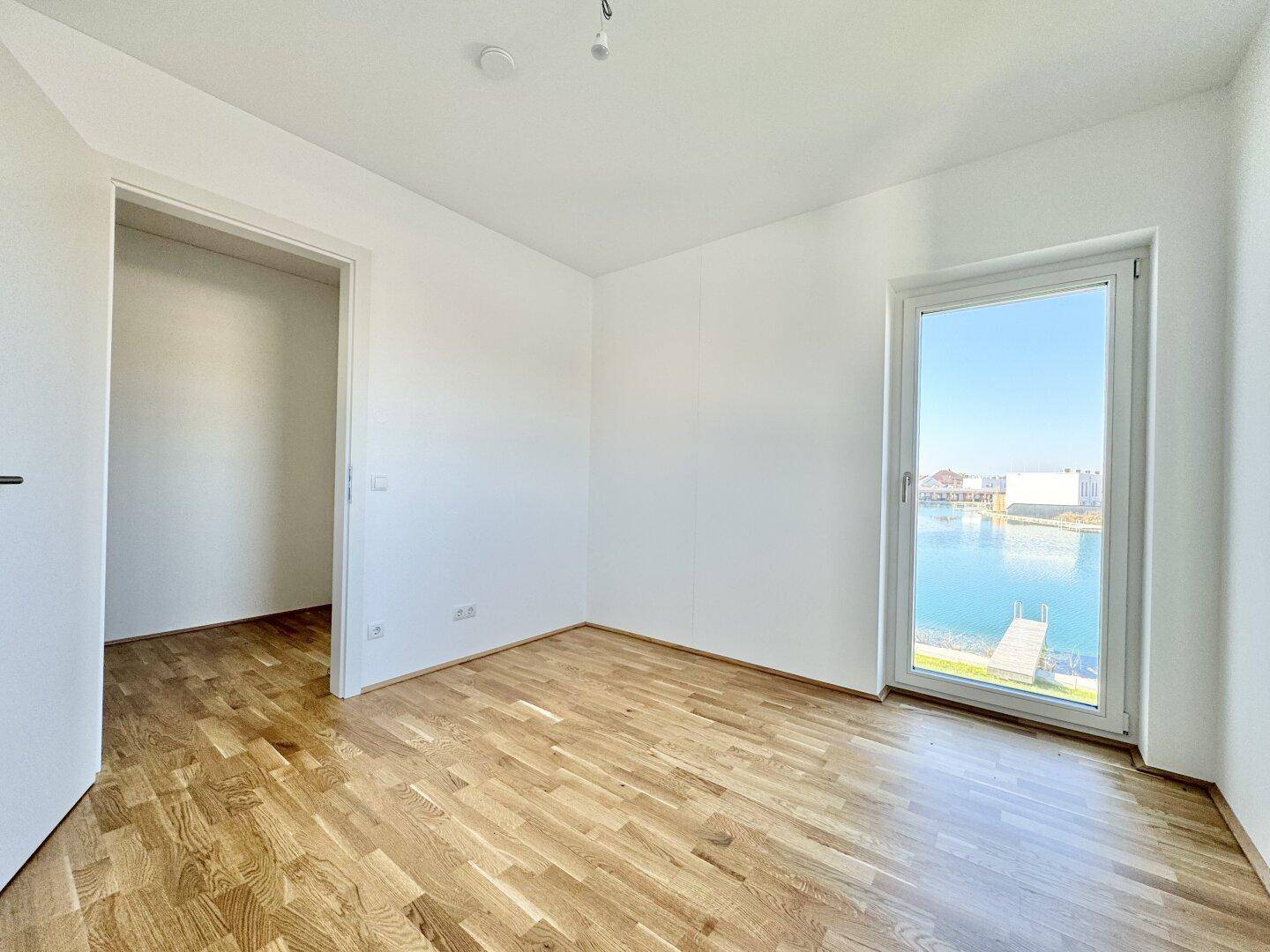 Leerer Raum mit Parkettboden und großem Fenster mit Blick auf den See.