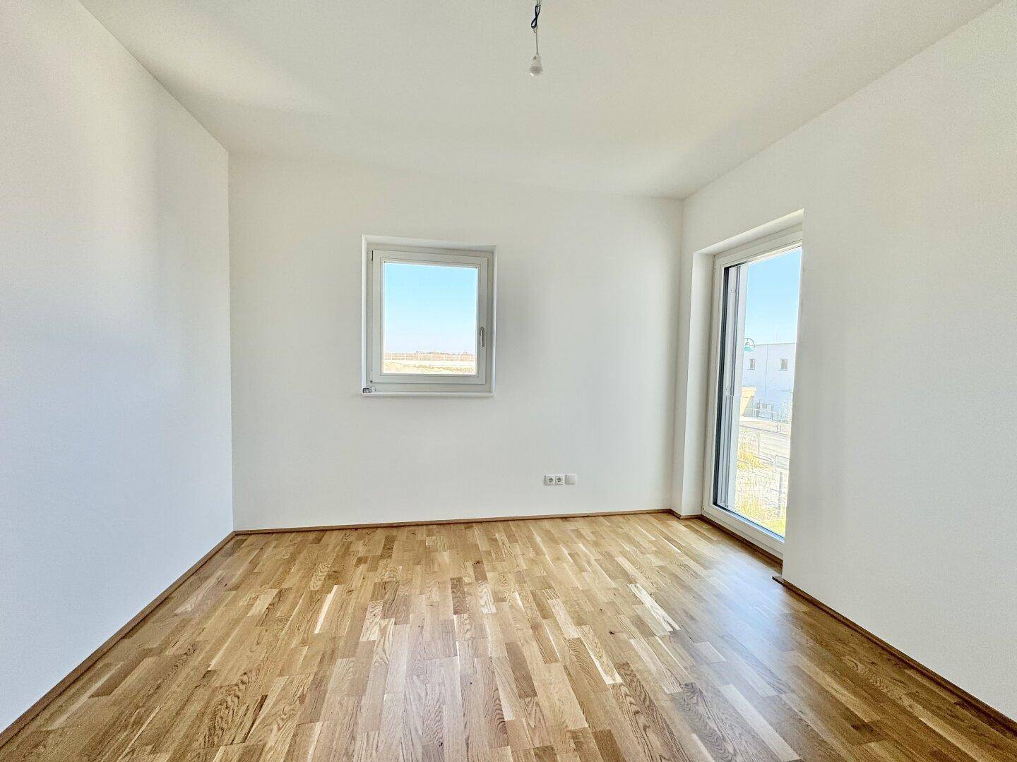 Geräumiger, heller Raum mit Parkettboden und zwei Fenstern.