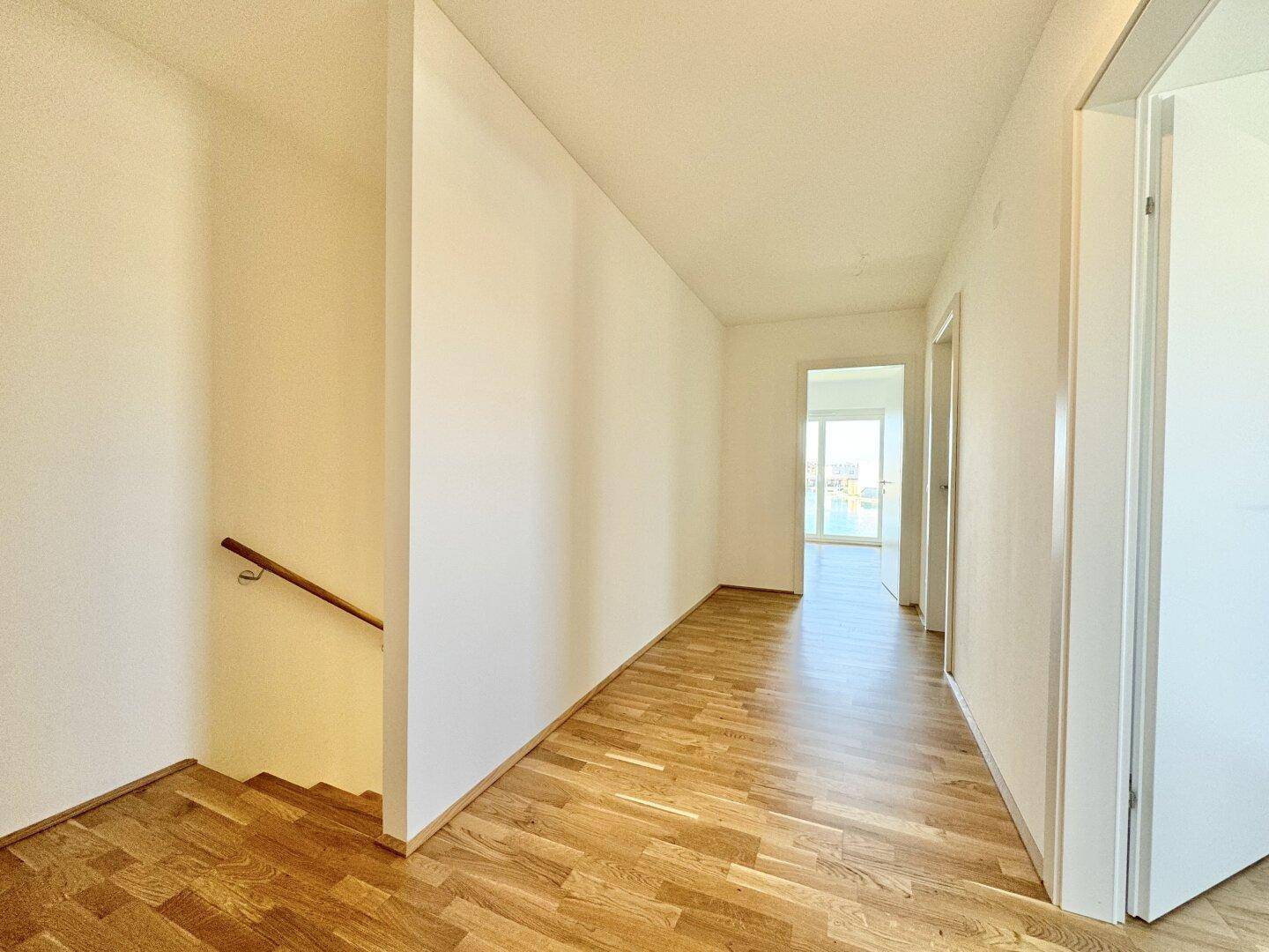 Heller Flur mit Holztreppe und Parkettboden, der die verschiedenen Räume verbindet.