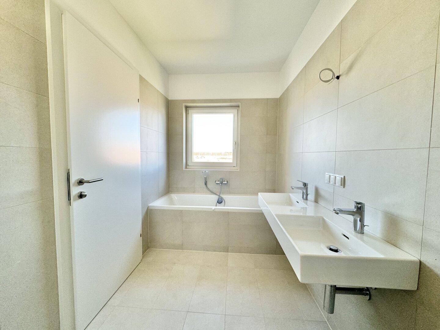 Modernes Badezimmer mit Doppelwaschbecken, Badewanne und Fenster für Tageslicht.