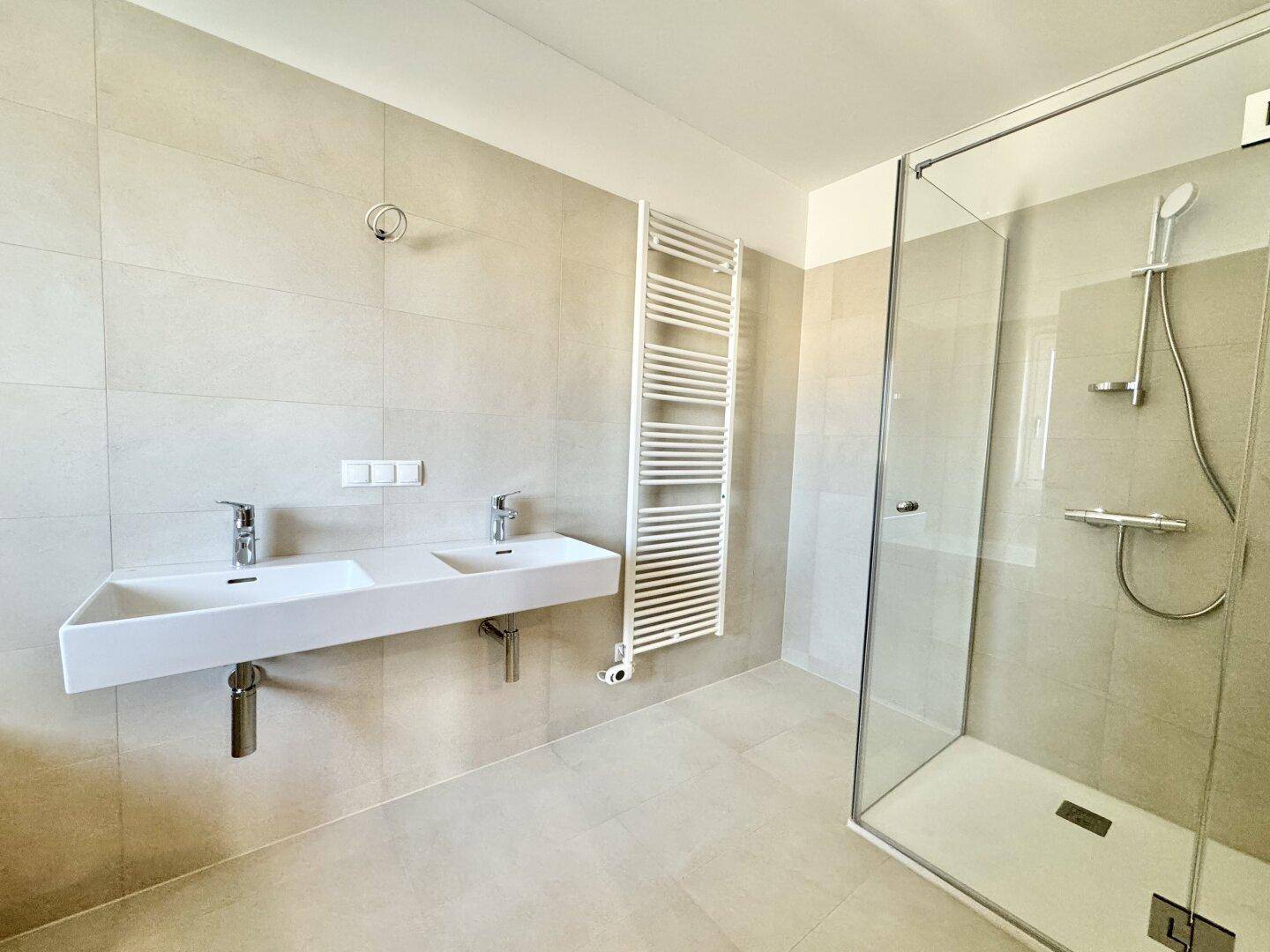 Modernes Badezimmer mit Doppelwaschbecken, begehbarer Dusche und beheiztem Handtuchhalter.