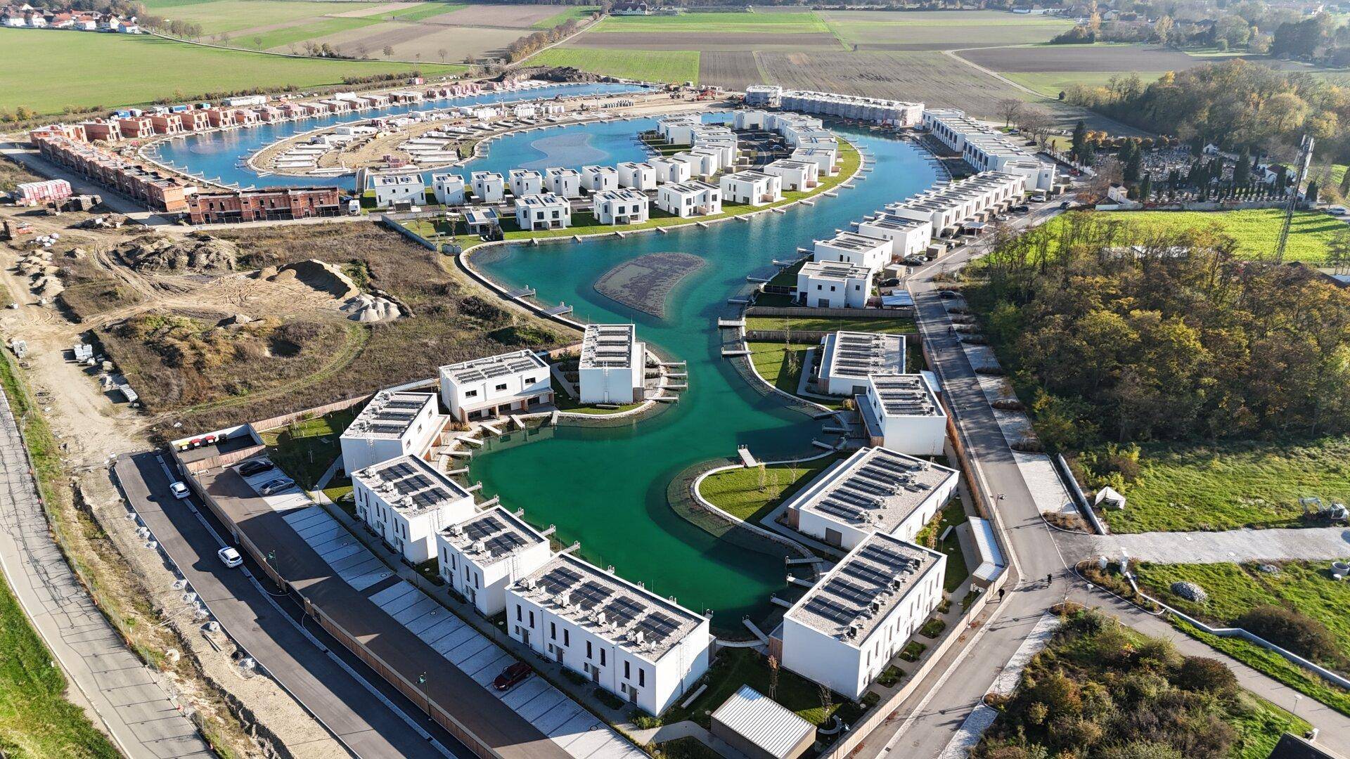 Luftaufnahme der modernen Wohnanlage mit Häusern, die sich um einen künstlichen See gruppieren.