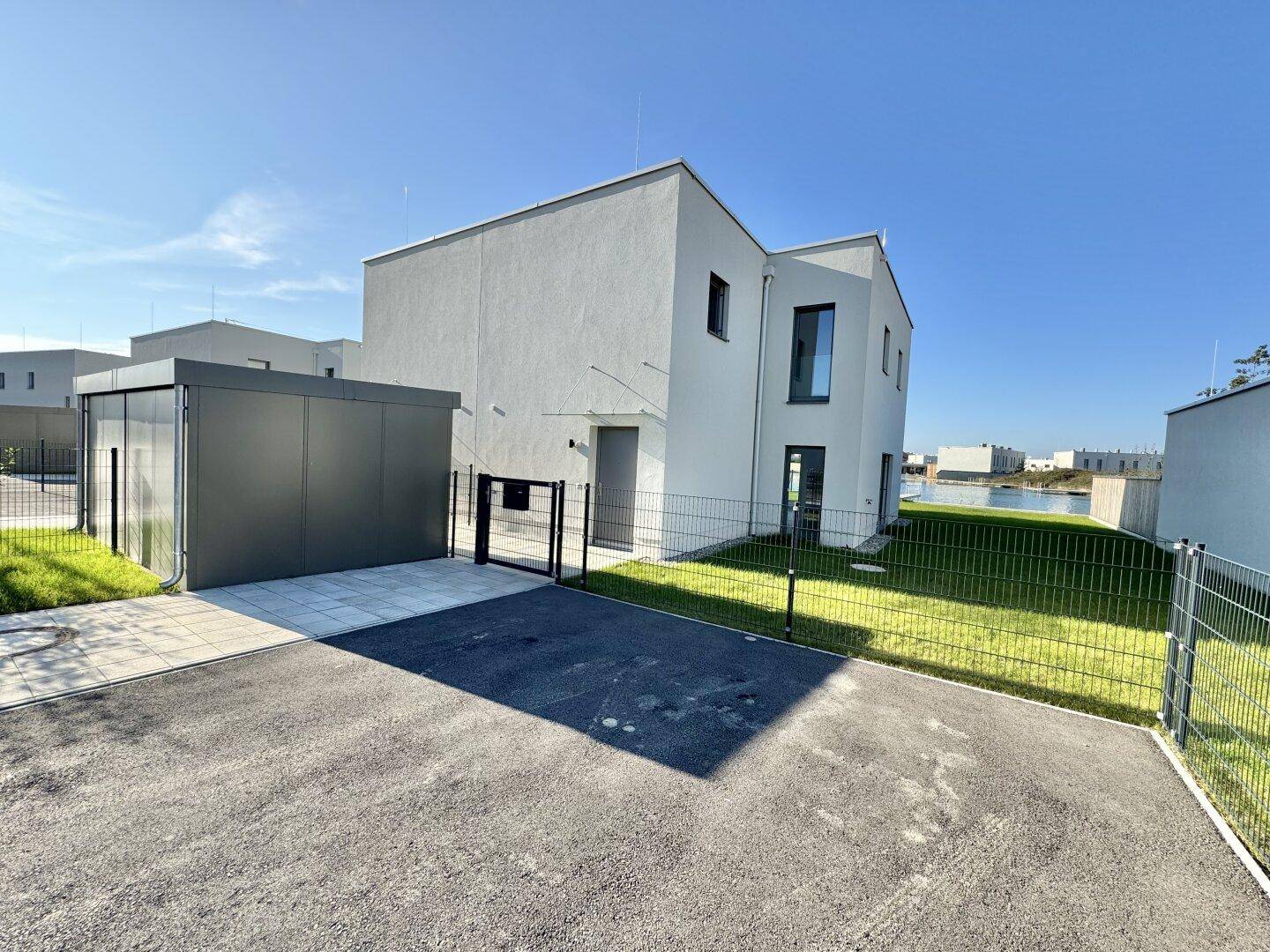 Vorderansicht des modernen Hauses mit Carport, Einfahrt und Blick auf den See im Hintergrund.