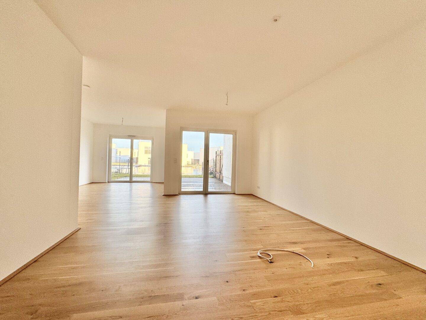 Heller, leerer Wohnraum mit Eichenparkettboden und großen Schiebetüren zur Terrasse.