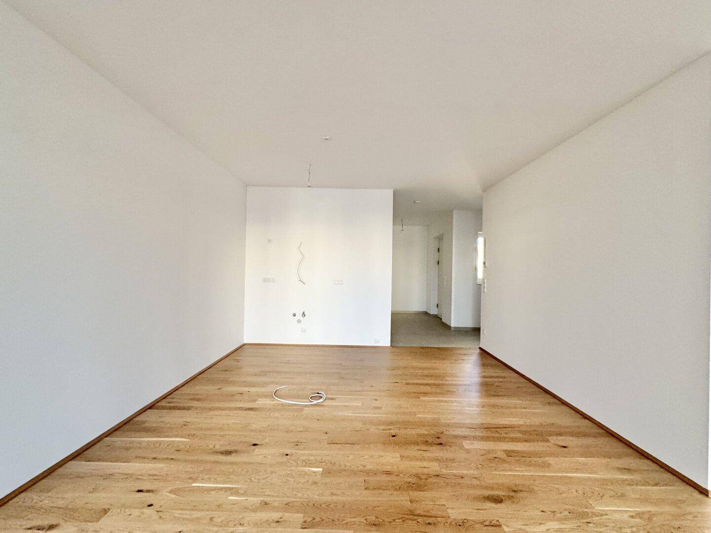 Offener Wohnbereich mit hellem Parkettboden und Übergang zu einem Flur.