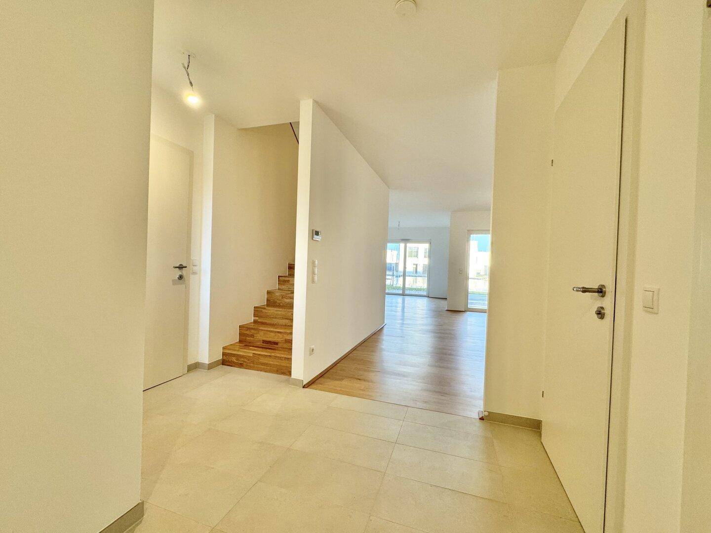 Geräumiger Flur mit Fliesenboden und einer Holztreppe, die in die oberen Stockwerke führt.