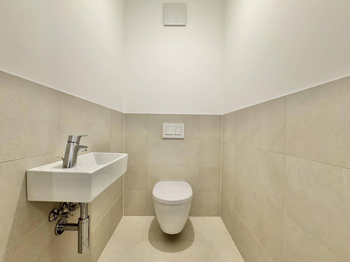 Modernes Gäste-WC mit wandhängender Toilette, kleinem Waschbecken und beigefarbenen Fliesen.