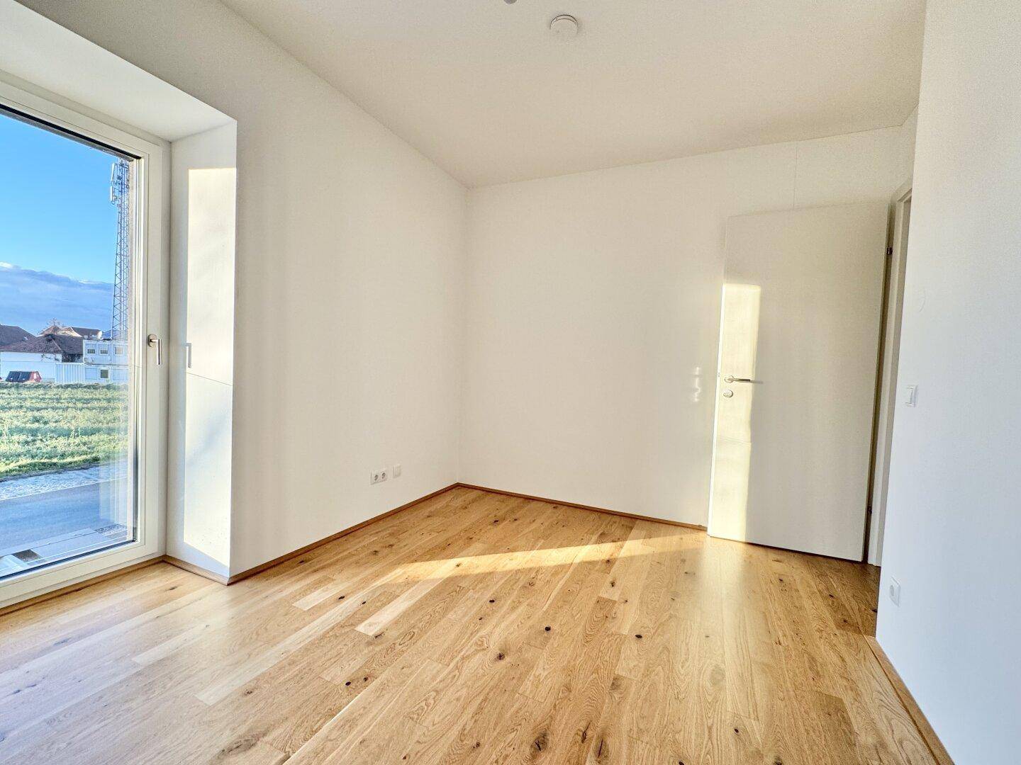 Geräumiges Schlafzimmer mit Eichenparkett und Zugang zu einem Außenbereich durch eine Fenstertür.