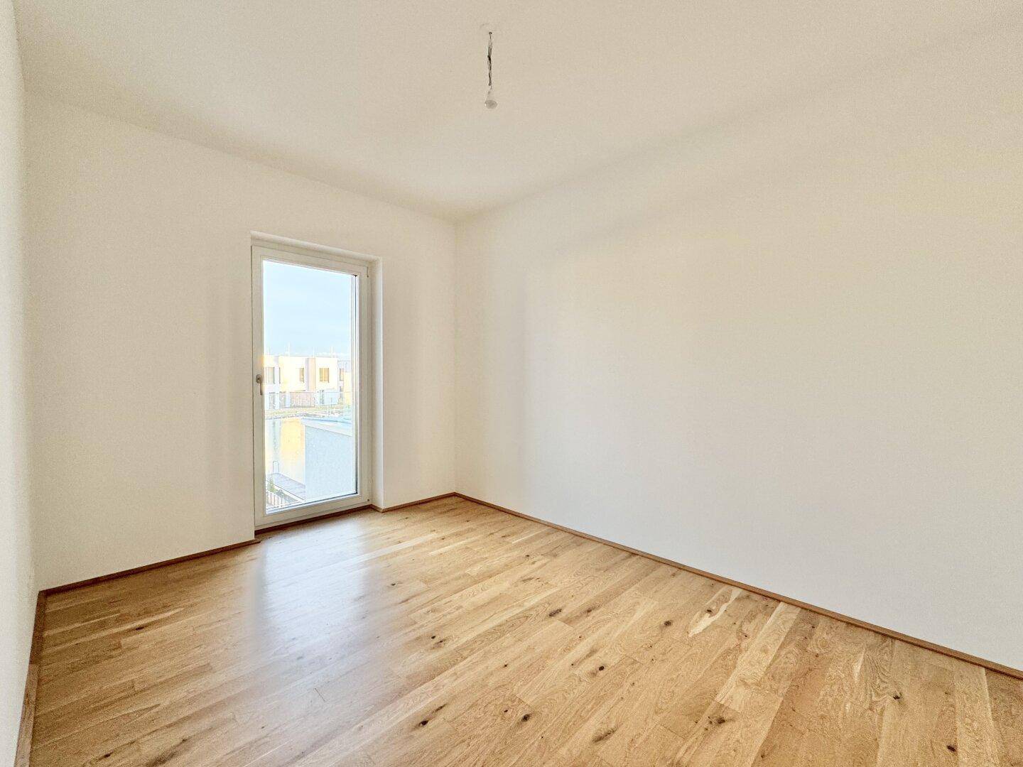 Helles Zimmer mit Eichenparkettboden und einem hohen Fenster, ideal als Schlaf- oder Arbeitszimmer.