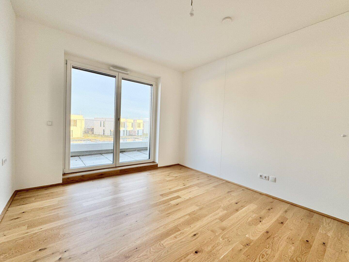 Schlafzimmer mit Eichenparkettboden und großen Schiebetüren, die auf einen Balkon oder eine Terrasse führen.