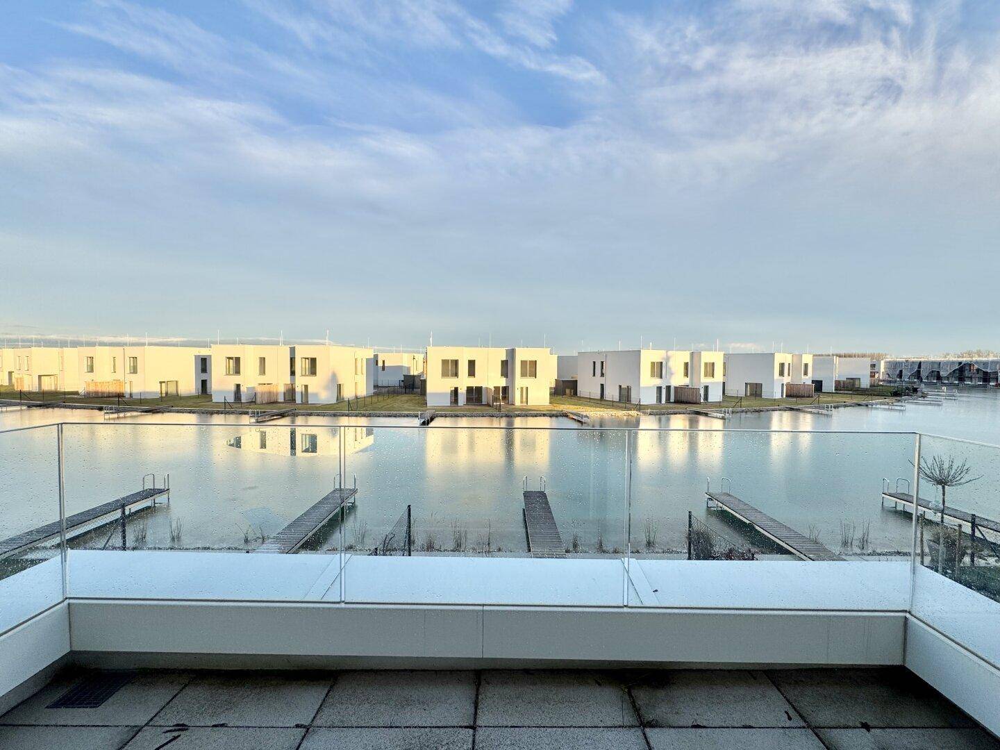 Geräumiger Balkon mit Glasgeländer und weitem Blick auf einen zugefrorenen See und moderne Häuser.