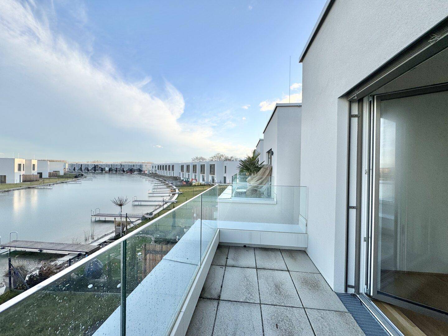 Großer Balkon mit Glasgeländer und Panoramablick auf den See und die umliegende moderne Bebauung.