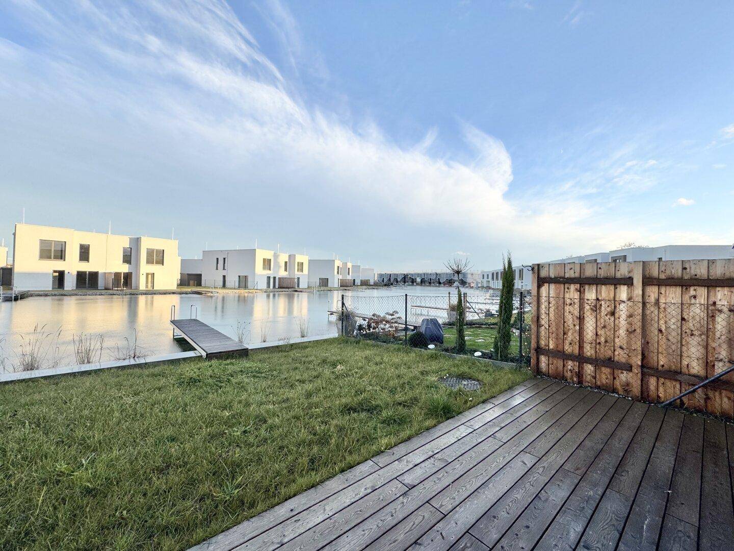 Privater Gartenbereich mit Holzterrasse und Rasenfläche, direkt am See gelegen mit Blick auf die Häuser.