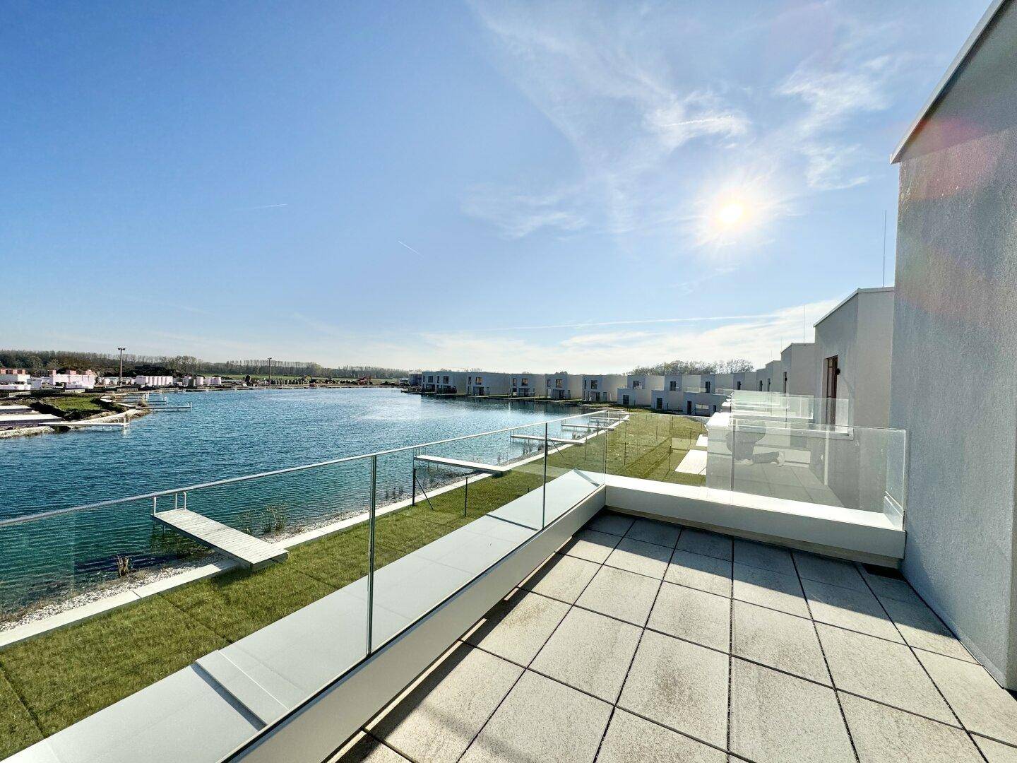 Große Dachterrasse mit Fliesenboden, Glasgeländer und Panoramablick über den See.