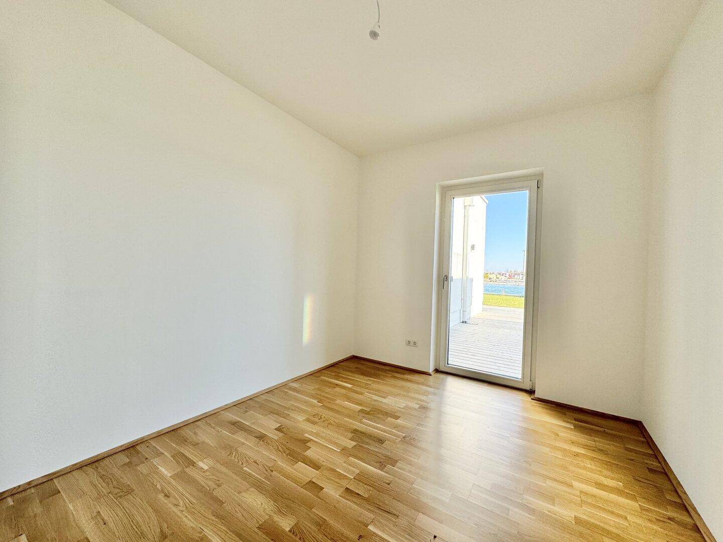 Helles Schlafzimmer mit Holzboden und Fenster mit Blick auf die Terrasse und den See.