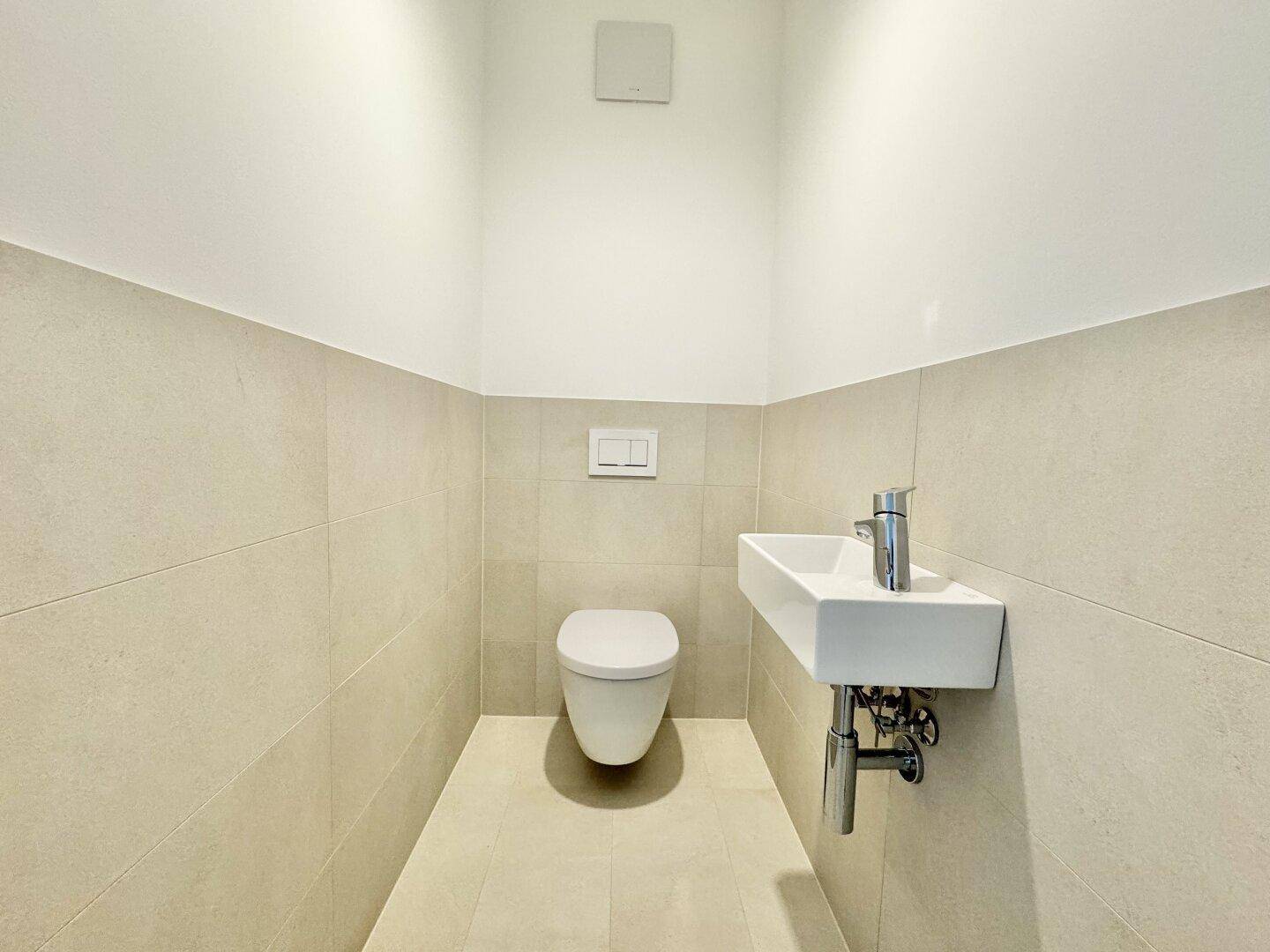 Kleines Gäste-WC mit Wand-WC, modernem Waschbecken und hellen Wandfliesen.