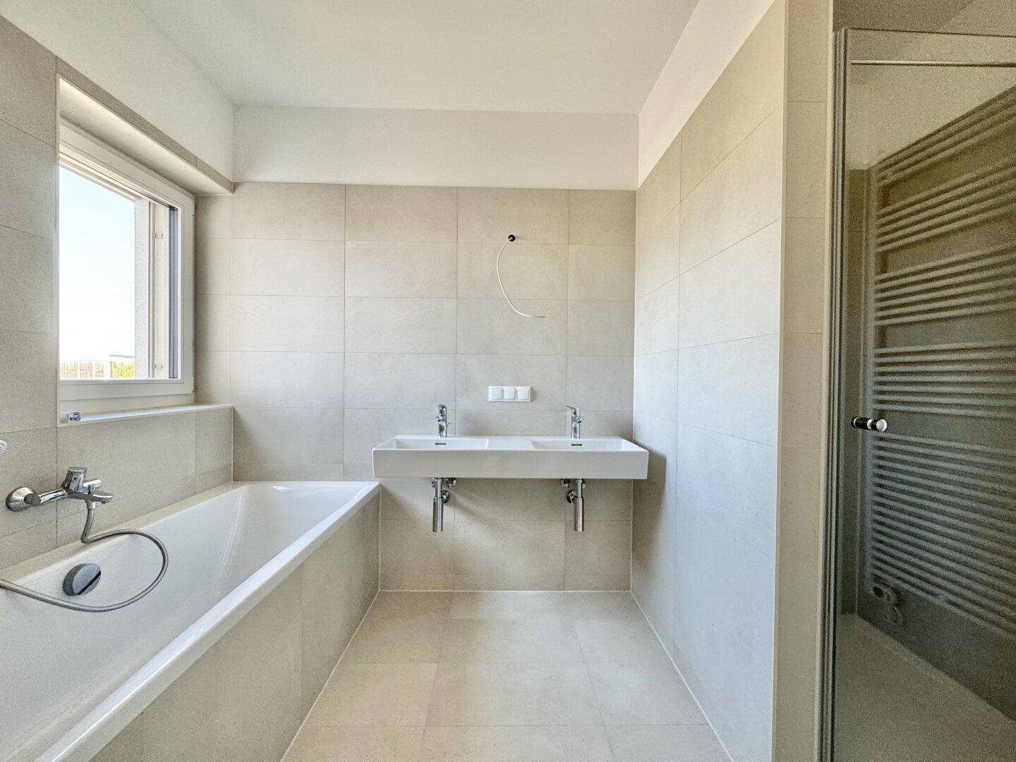 Modernes Badezimmer mit Doppelwaschbecken, Badewanne, Dusche und hellen Fliesen.