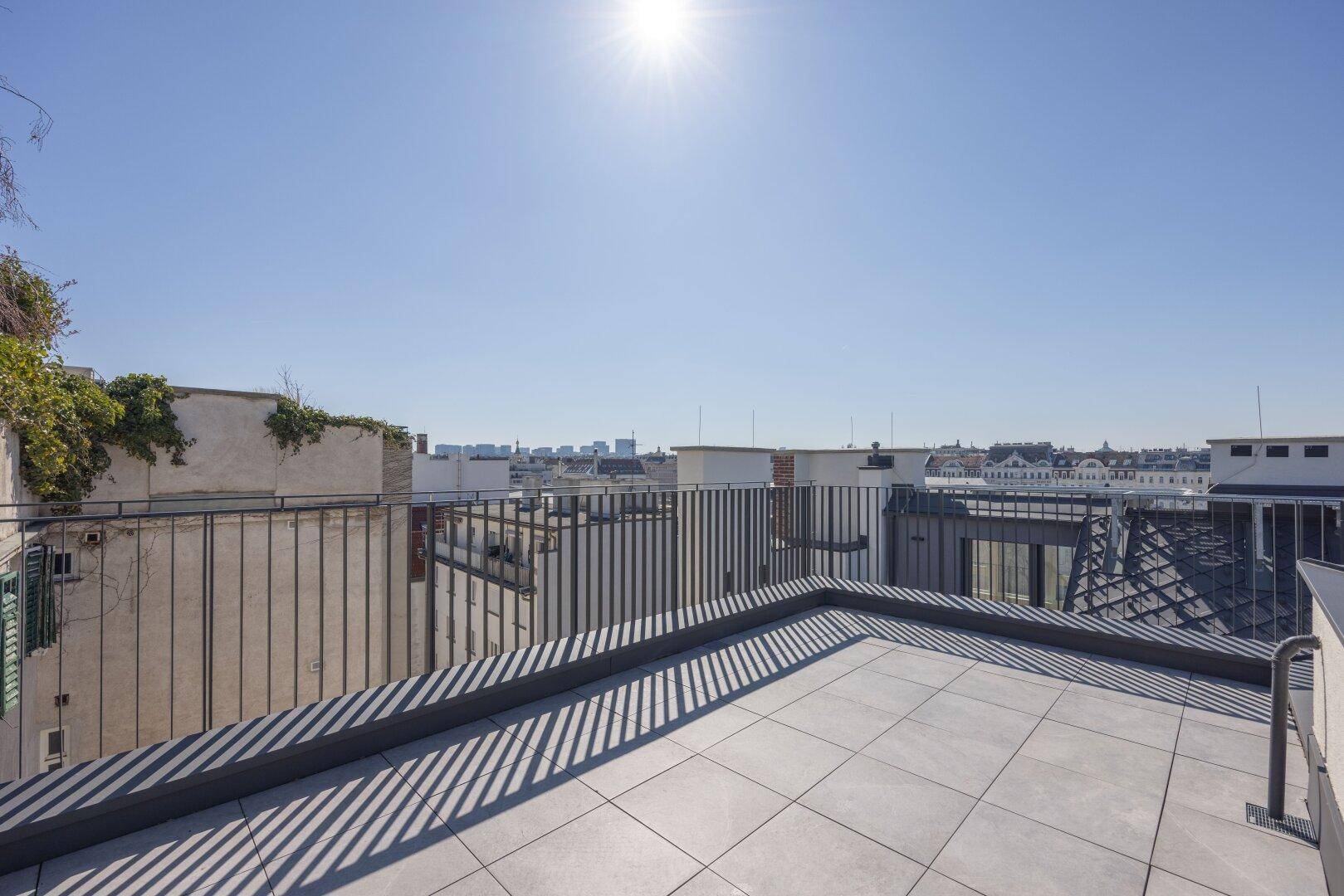 Helle Dachterrasse mit Fliesenboden und weitem Panorama über die Dächer der Stadt.