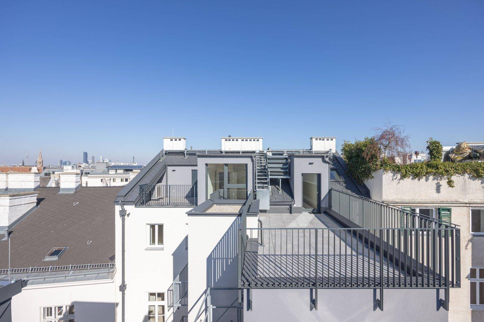 Moderne Dachaufbauten und Terrassenbereiche eines Wohngebäudes mit Blick auf die Stadt.