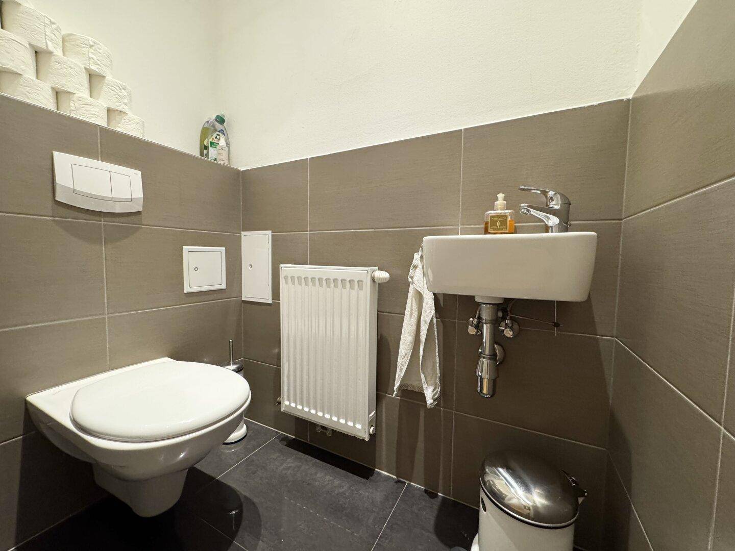 Separates Gäste-WC mit Wand-WC, kleinem Waschbecken und Heizkörper.