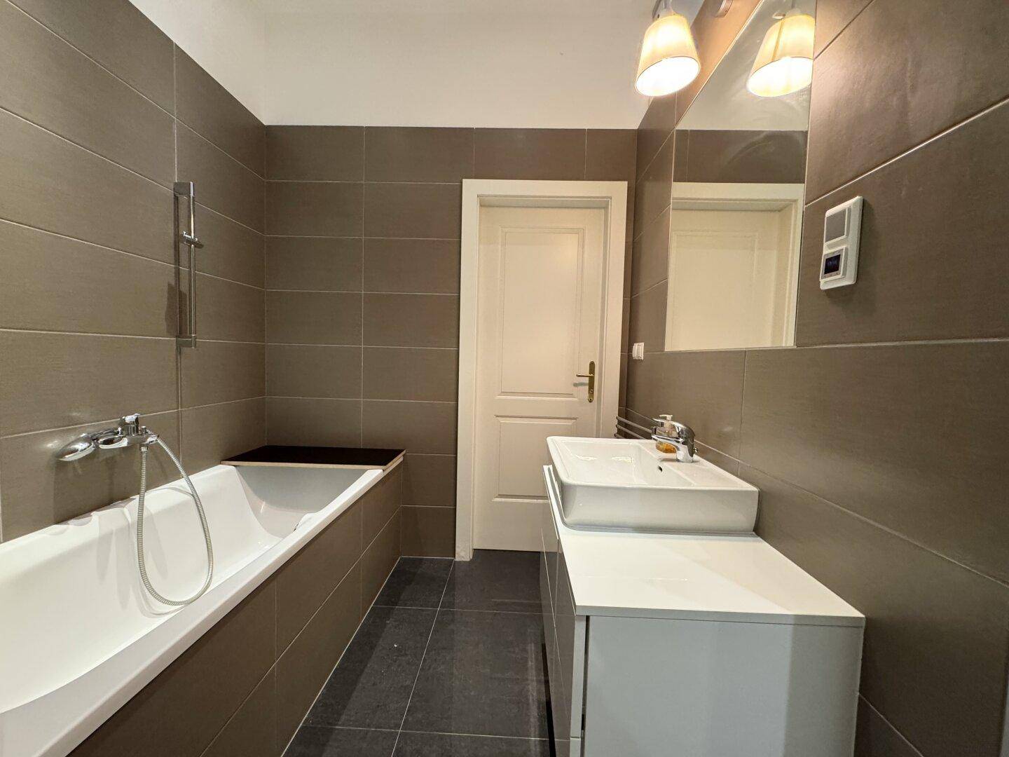 Modernes Badezimmer mit Badewanne, Waschtisch und grauen Fliesen.