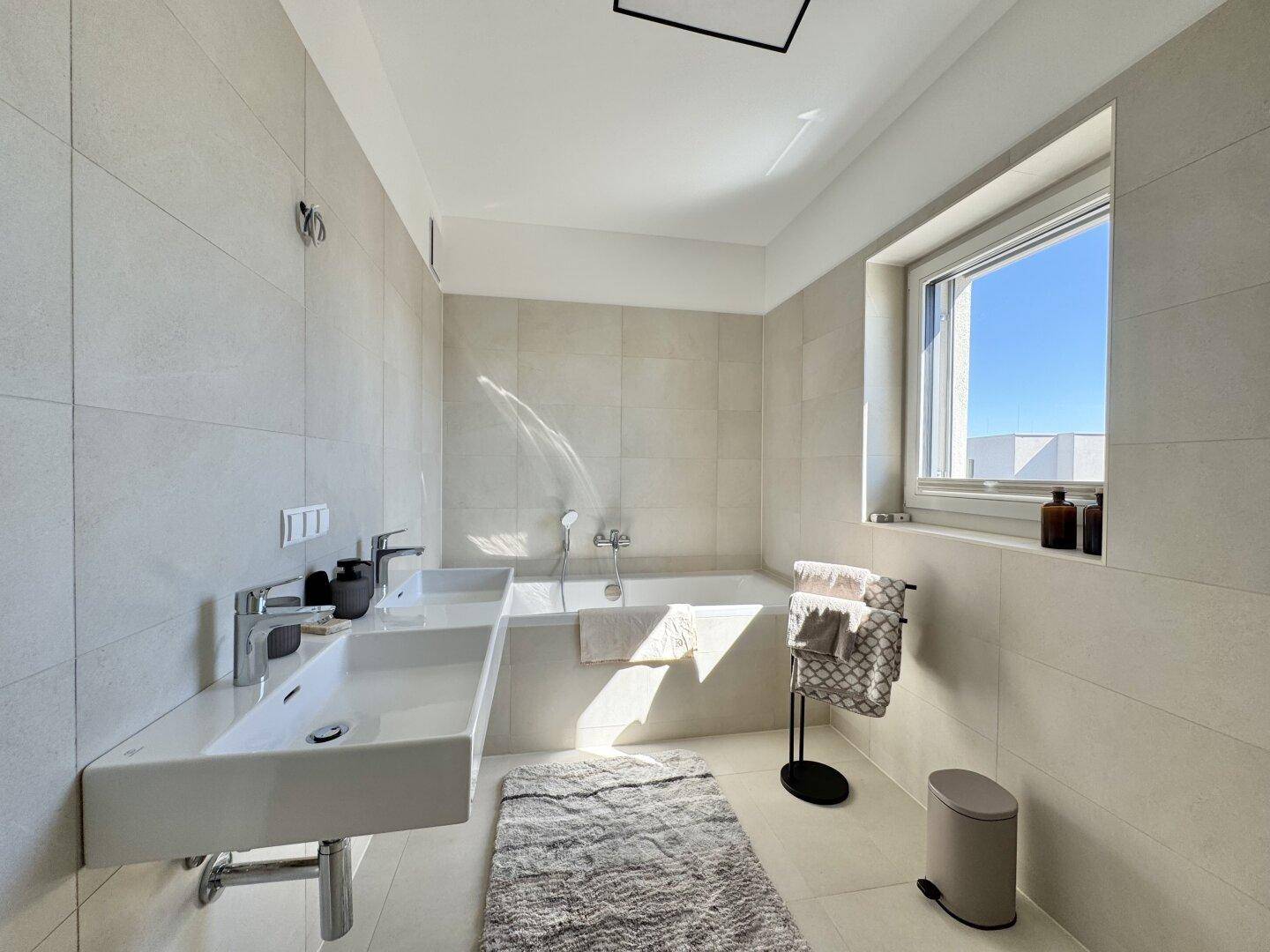 Modernes Badezimmer mit Doppelwaschbecken, Badewanne und großformatigen Fliesen.