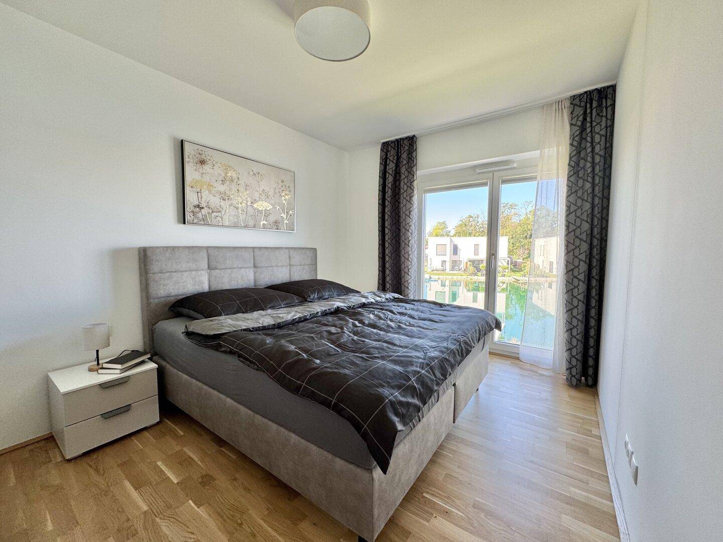 Geräumiges Schlafzimmer mit Doppelbett, Nachttisch und Zugang zum Balkon mit Seeblick.