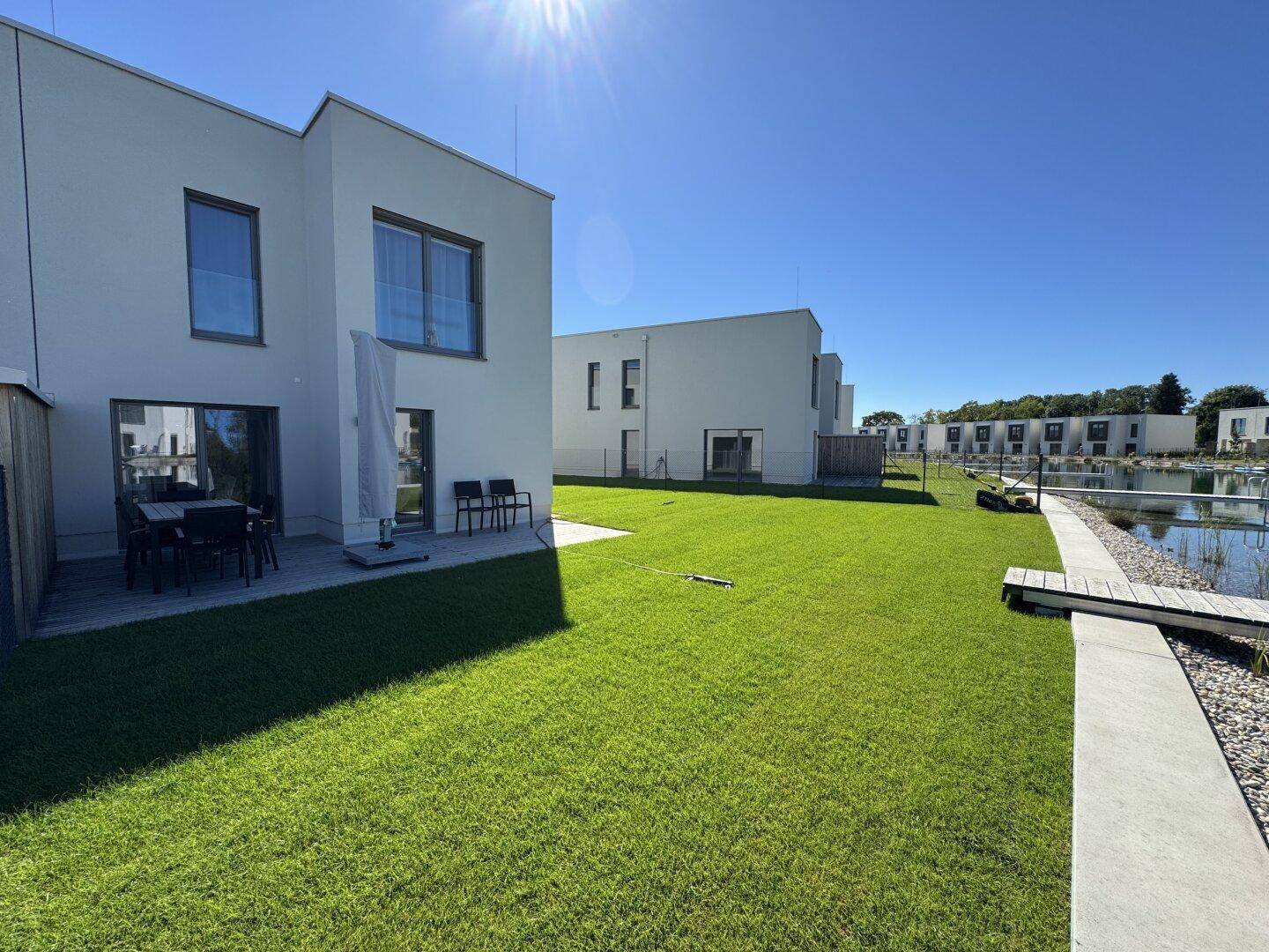 Gepflegter Garten mit Rasenfläche und Terrasse mit Sitzgelegenheiten am See.